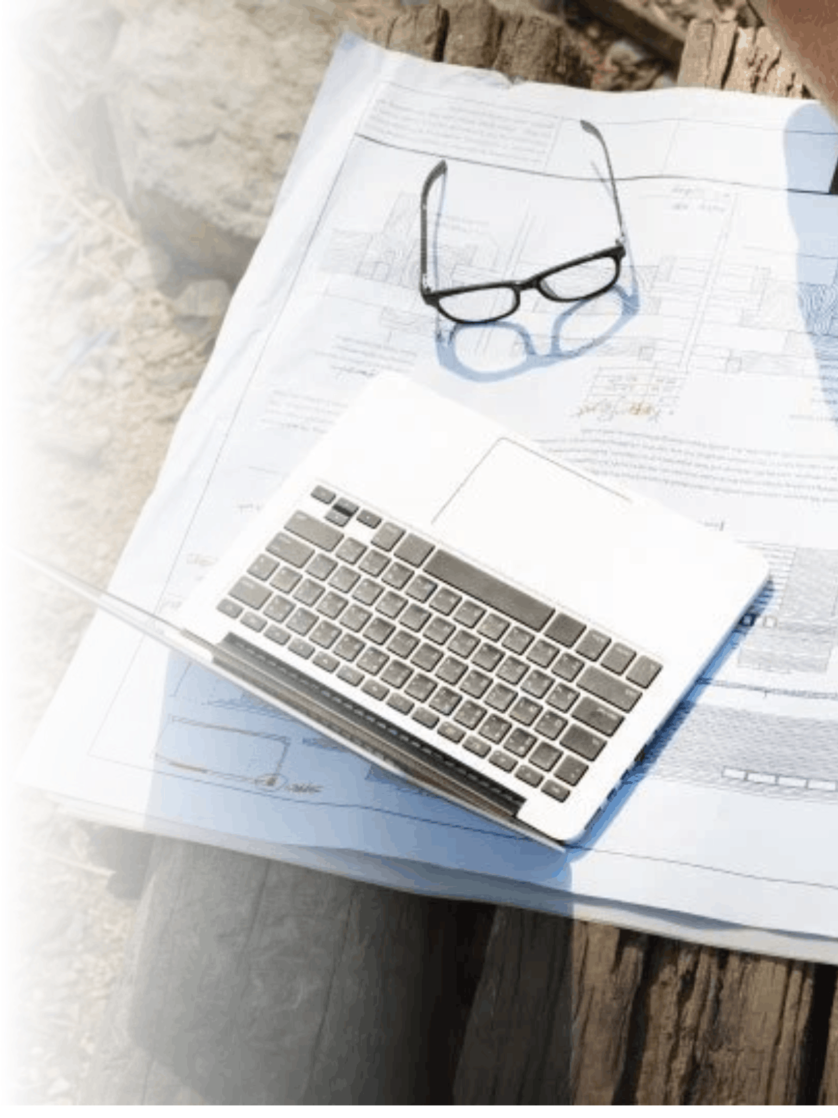 Lentes, computadora portátil y planos sobre una mesa de madera.