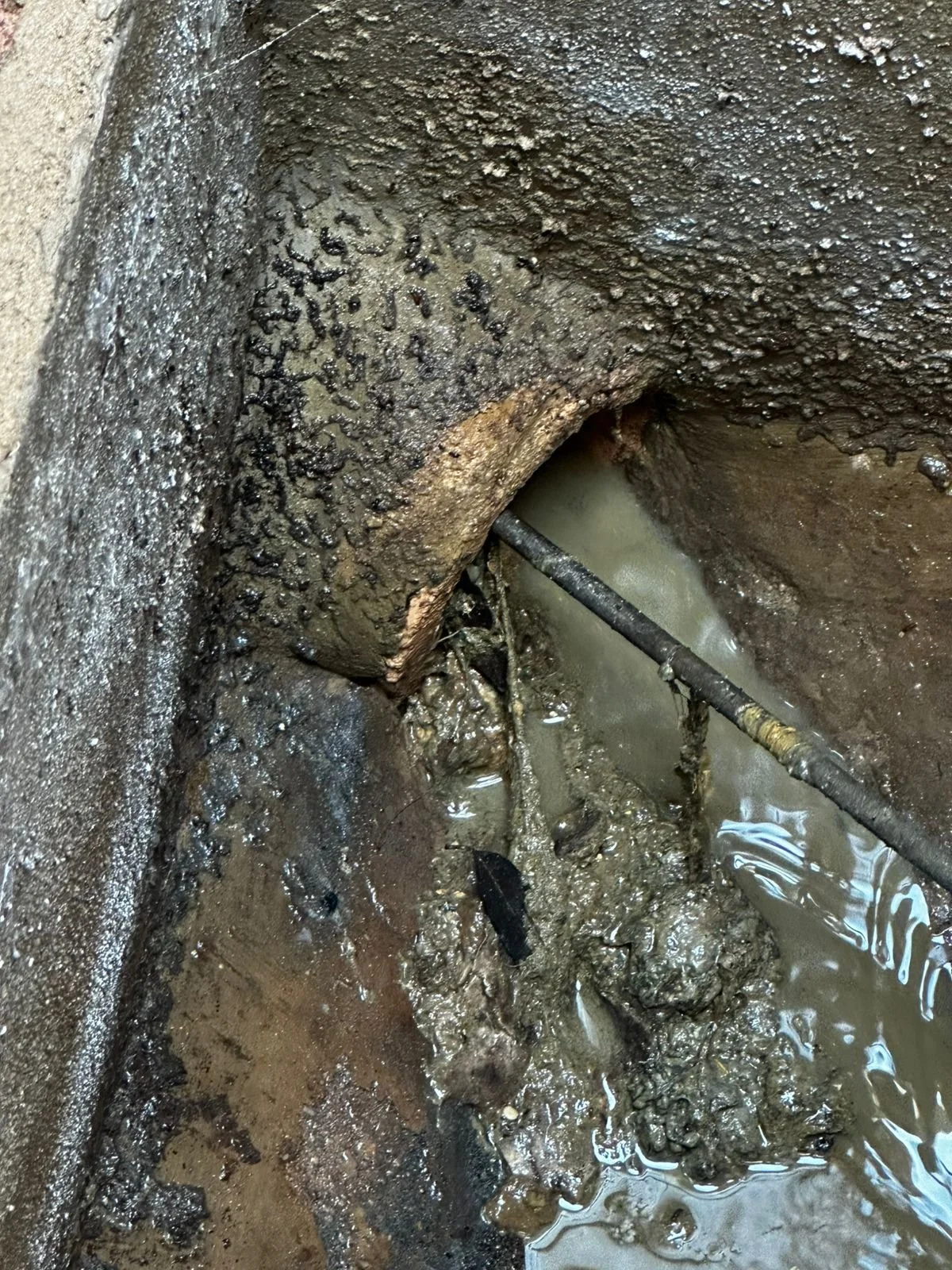 Tubería de desagüe obstruida con lodo y basura, rodeada de paredes sucias