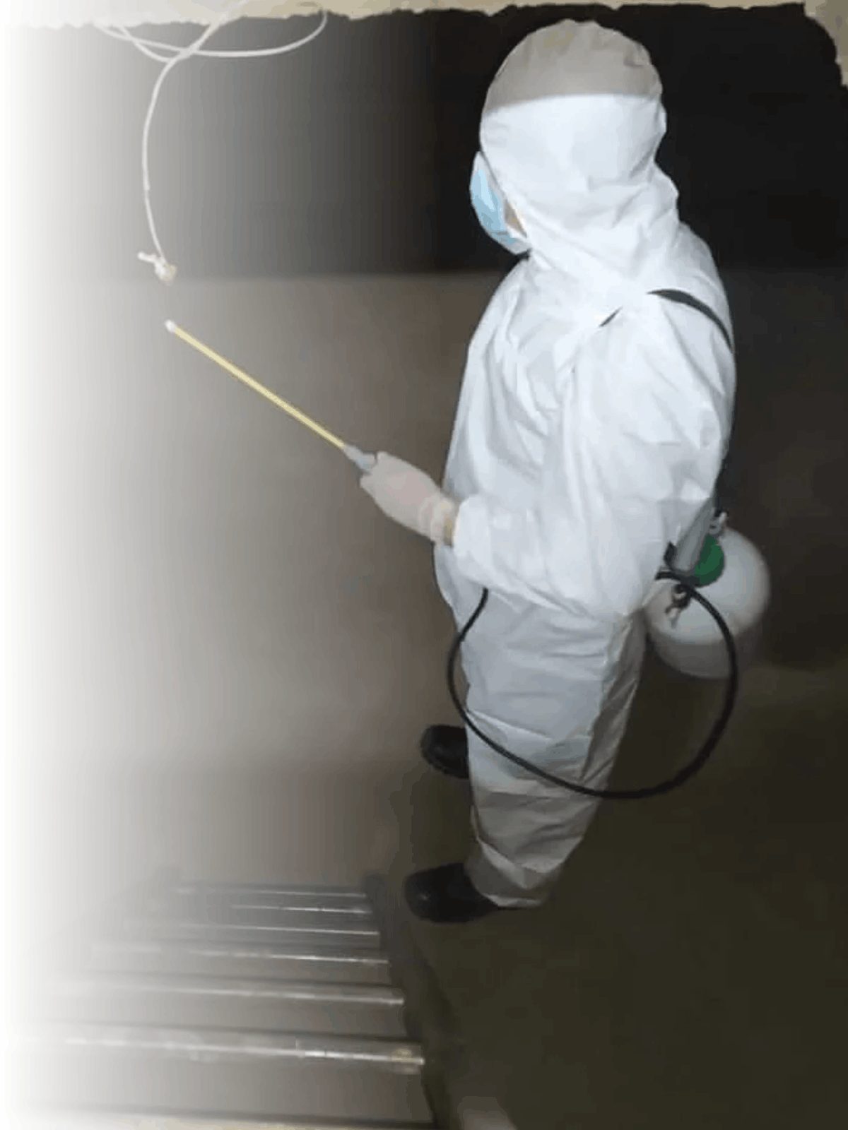 Persona con traje protector y máscara quitando superficies con equipo de desinfección