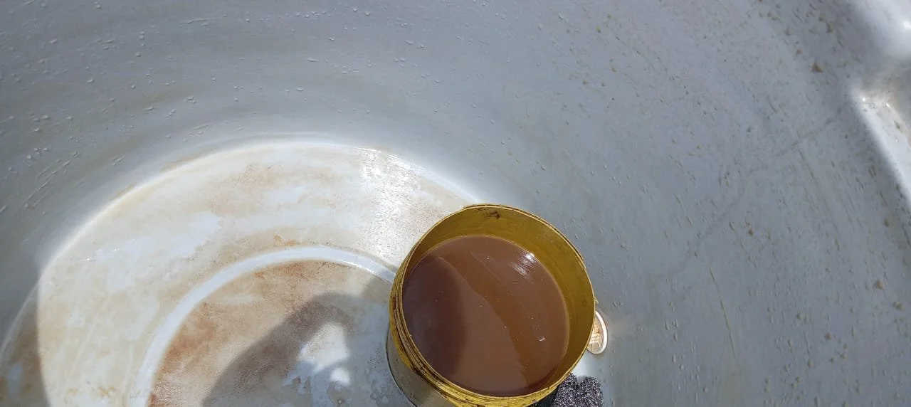 Cubo amarillo con agua marrón en el interior, dentro de un recipiente metálico con superficie sucia y desgaste.