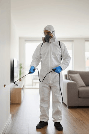 Persona con equipo de protección limpiando una superficie en una sala de estar moderna.