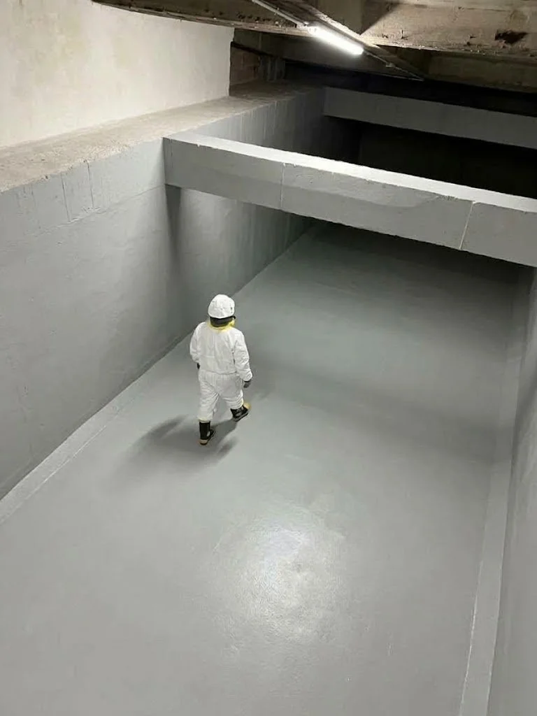 Persona vestida con uniforme de protección caminando en un tanque subterráneo con paredes y pisos recién limpiado