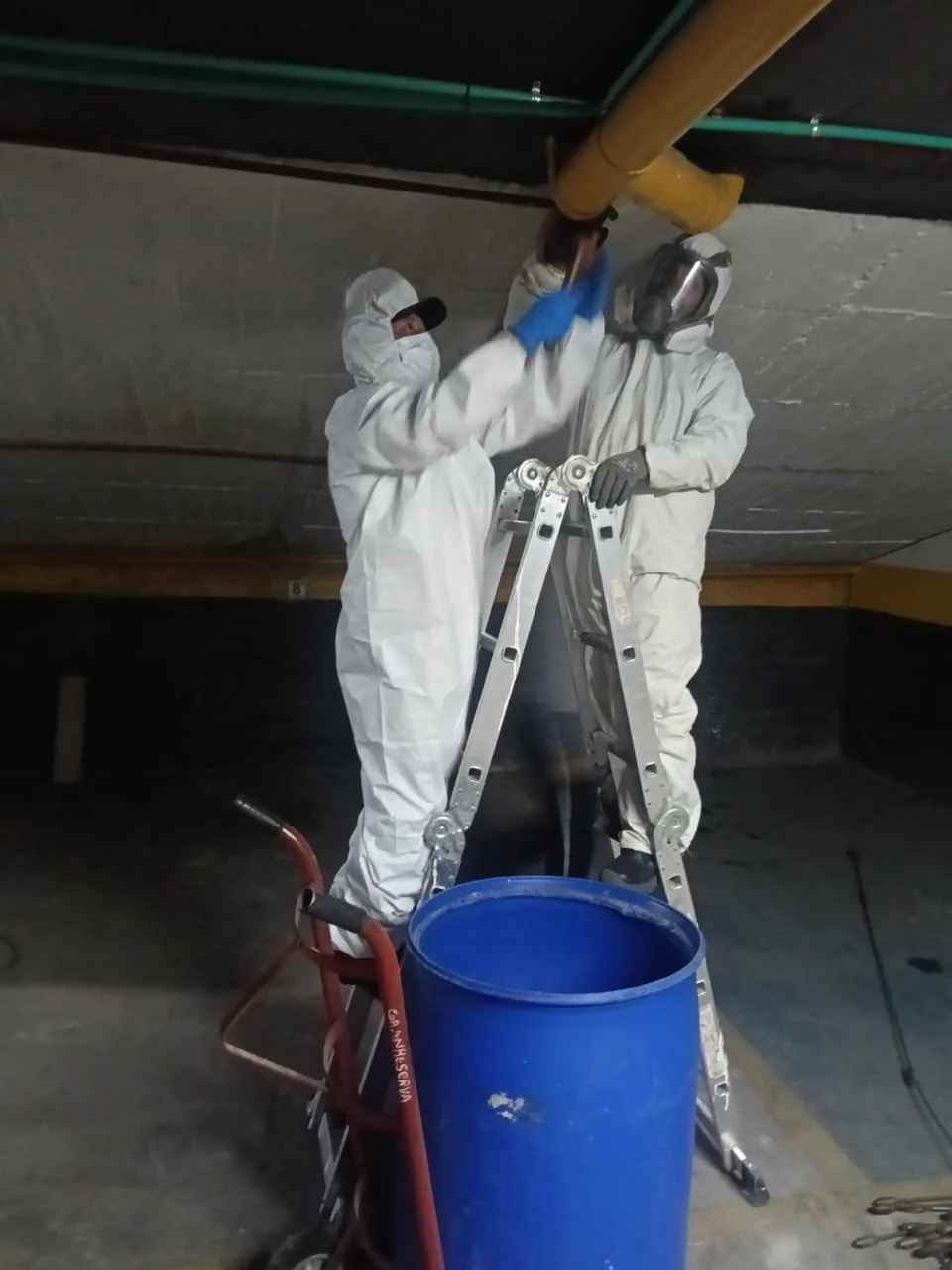 Dos trabajadores con trajes protectores y máscaras de protección mientras realizan un sondeo a un edificio