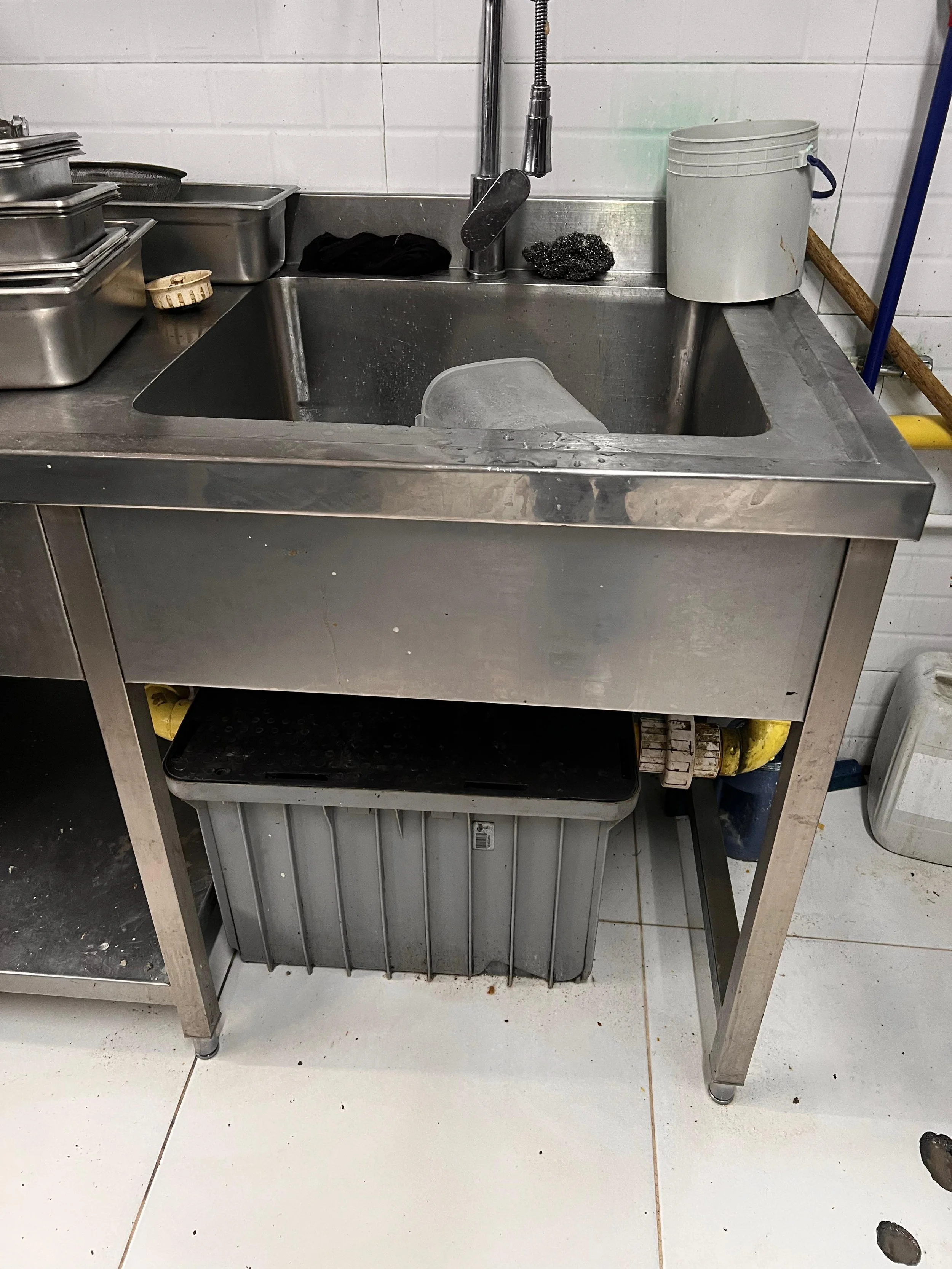 Lavaplatos de acero inoxidable en una cocina, con algunos objetos de limpieza y utensilios alrededor.