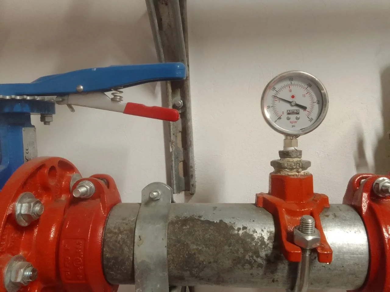 Tubería de metal con presión en un manómetro y una válvula hidráulica en un entorno industrial.