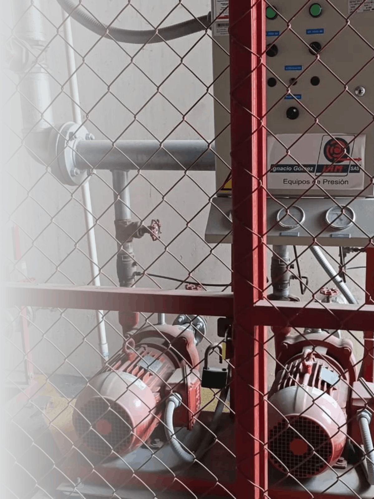 Equipo de presión industrial con motores y componentes metálicos, protegido por una cerca de malla metálica, en un entorno de industria.