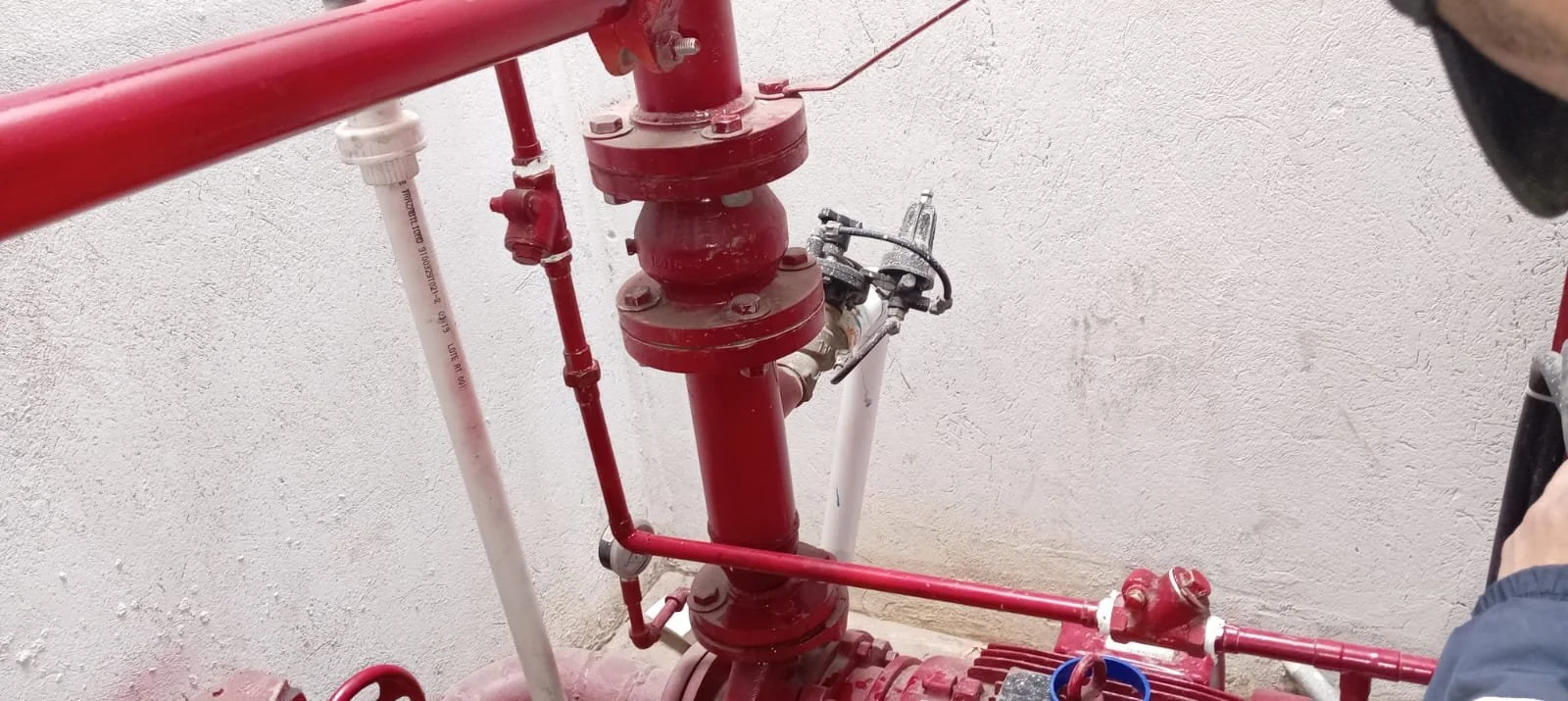 Sistema de tuberías y válvula de agua rojas y blancas en una pared blanca.