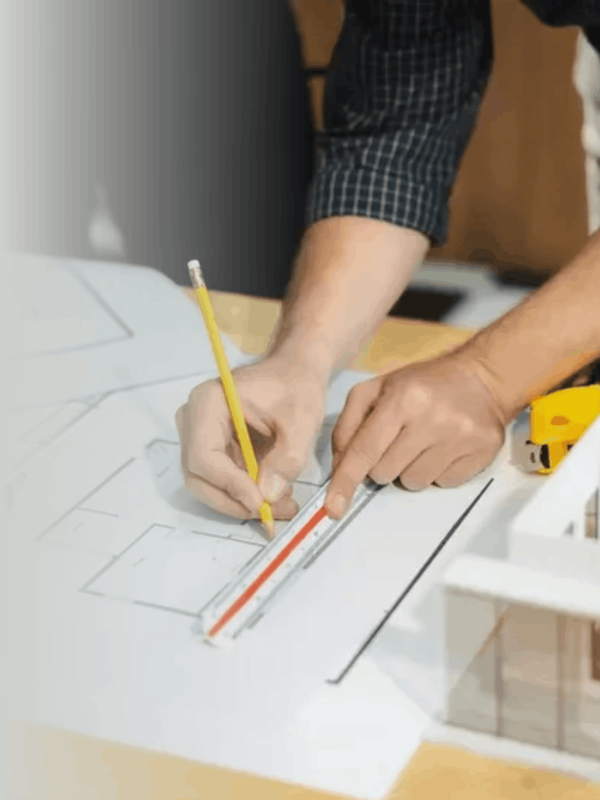 Persona dibujando planos arquitectónicos con regla y lápiz en escritorio.