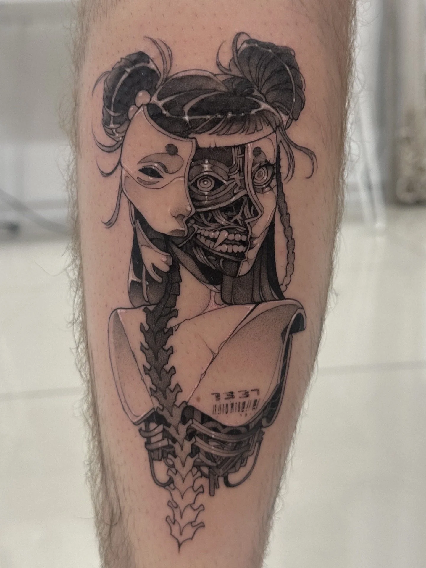 Tattoo of a woman with mechanical and robotic elements, holding a barcode label. The tattoo is in black and gray ink.