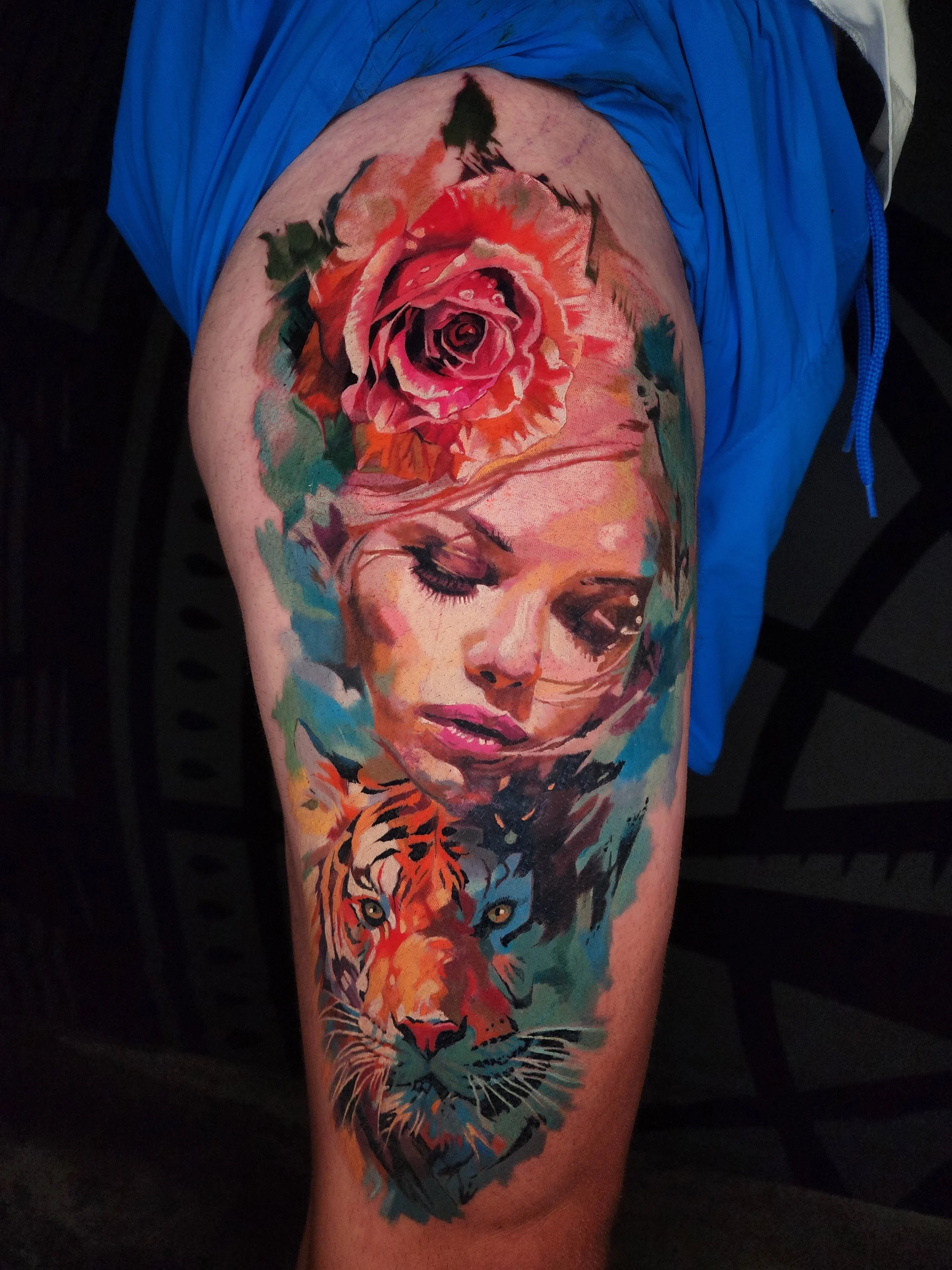 Tattoo of a woman's face with closed eyes, a rose above her head, and a tiger at the bottom, in a vibrant, colorful style.