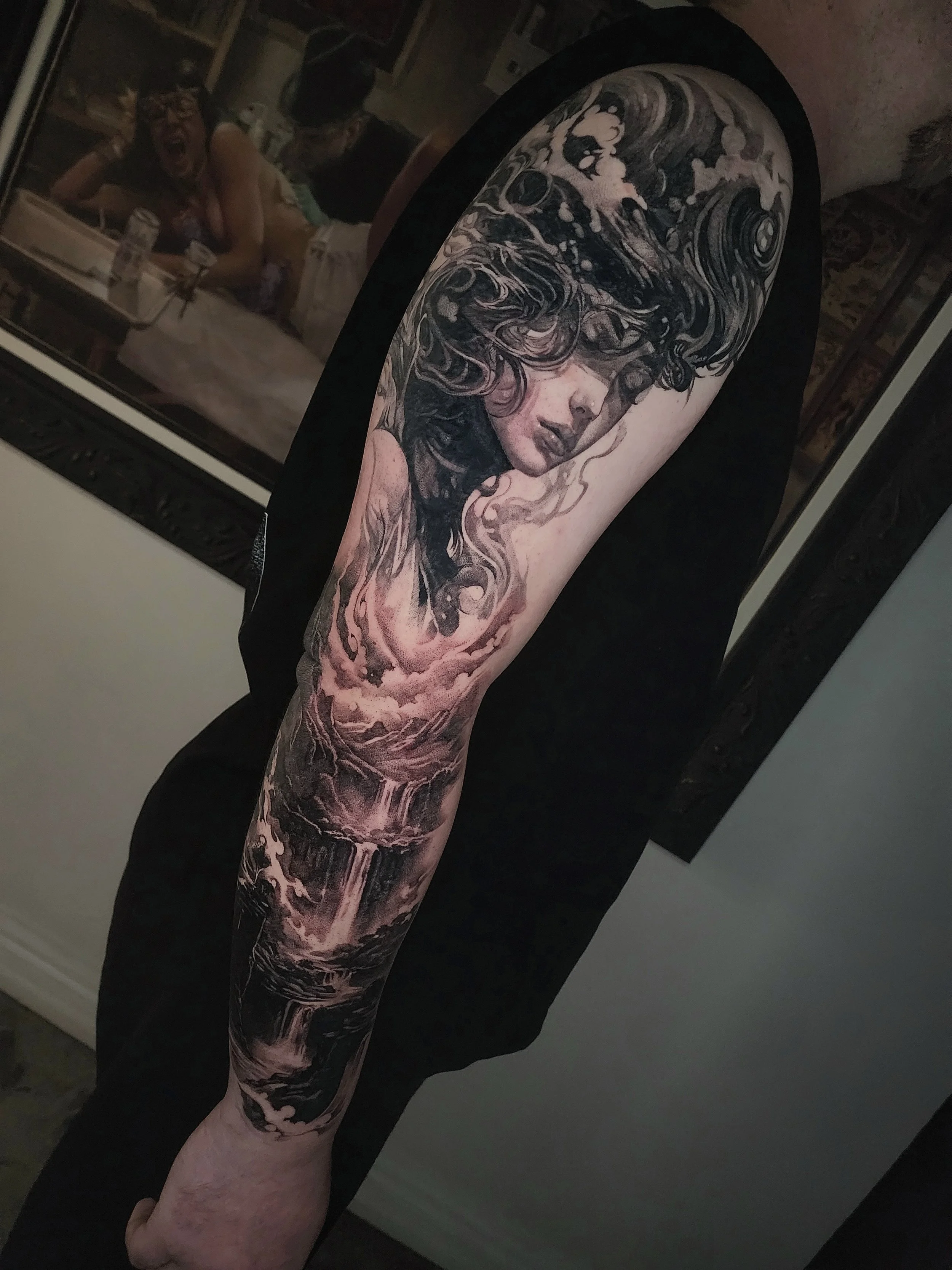 A detailed black and gray tattoo sleeve depicting a woman's face with flowing hair and a waterfall scene on the lower arm.