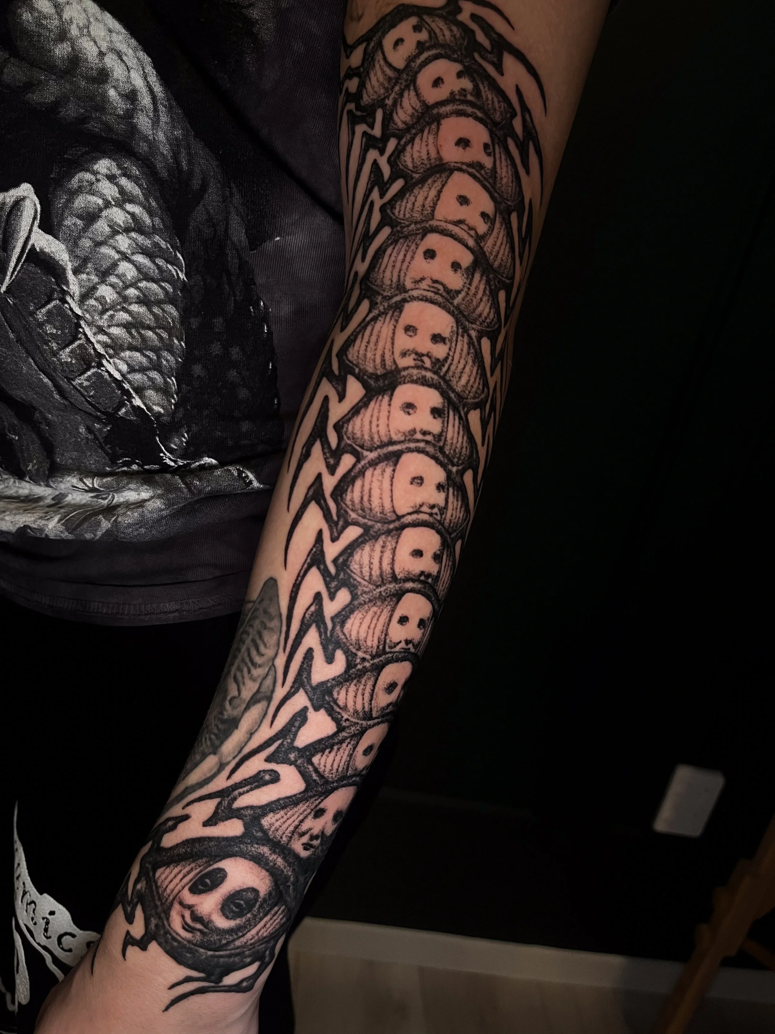 A tattoo of multiple faces in a vertical line on a person's arm, featuring a woman with long hair and a serious expression at the bottom.