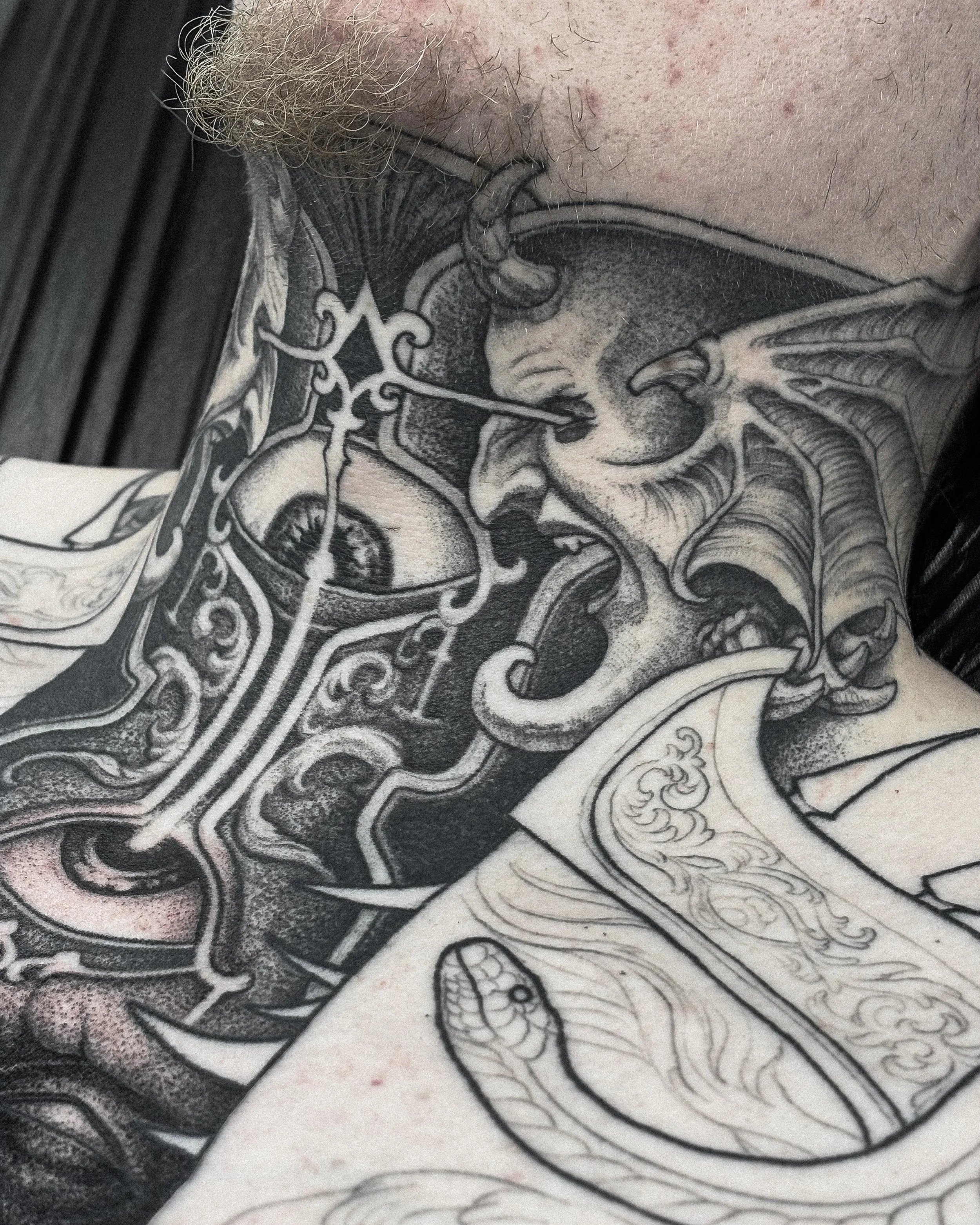 Black and gray tattoo of a screaming, monstrous face with sharp teeth and tentacle-like appendages, intertwined with ornate designs and a snake.