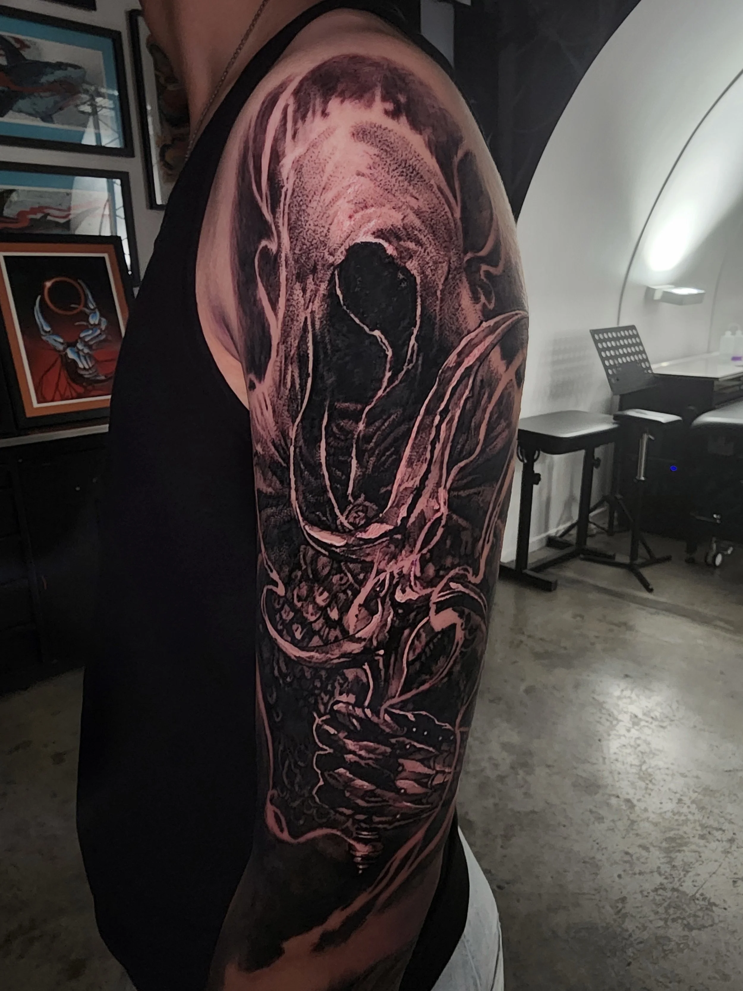 Tattoo of a screaming skull with a hood on a person's upper arm in black and gray ink.