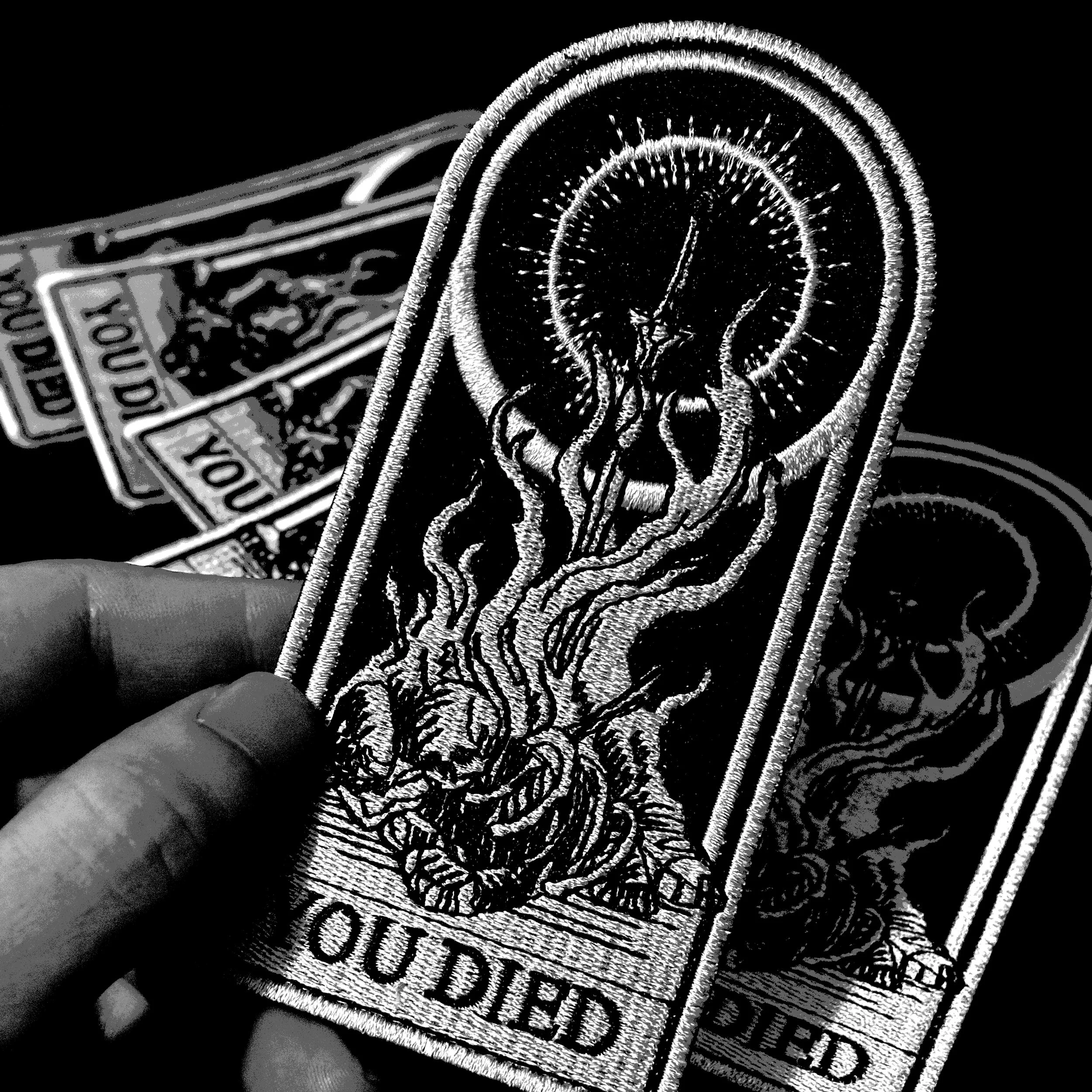 A collection of embroidered patches featuring a tree with roots and a circular pattern, with the word 'OUTDATED' at the bottom, held in a person's hand.