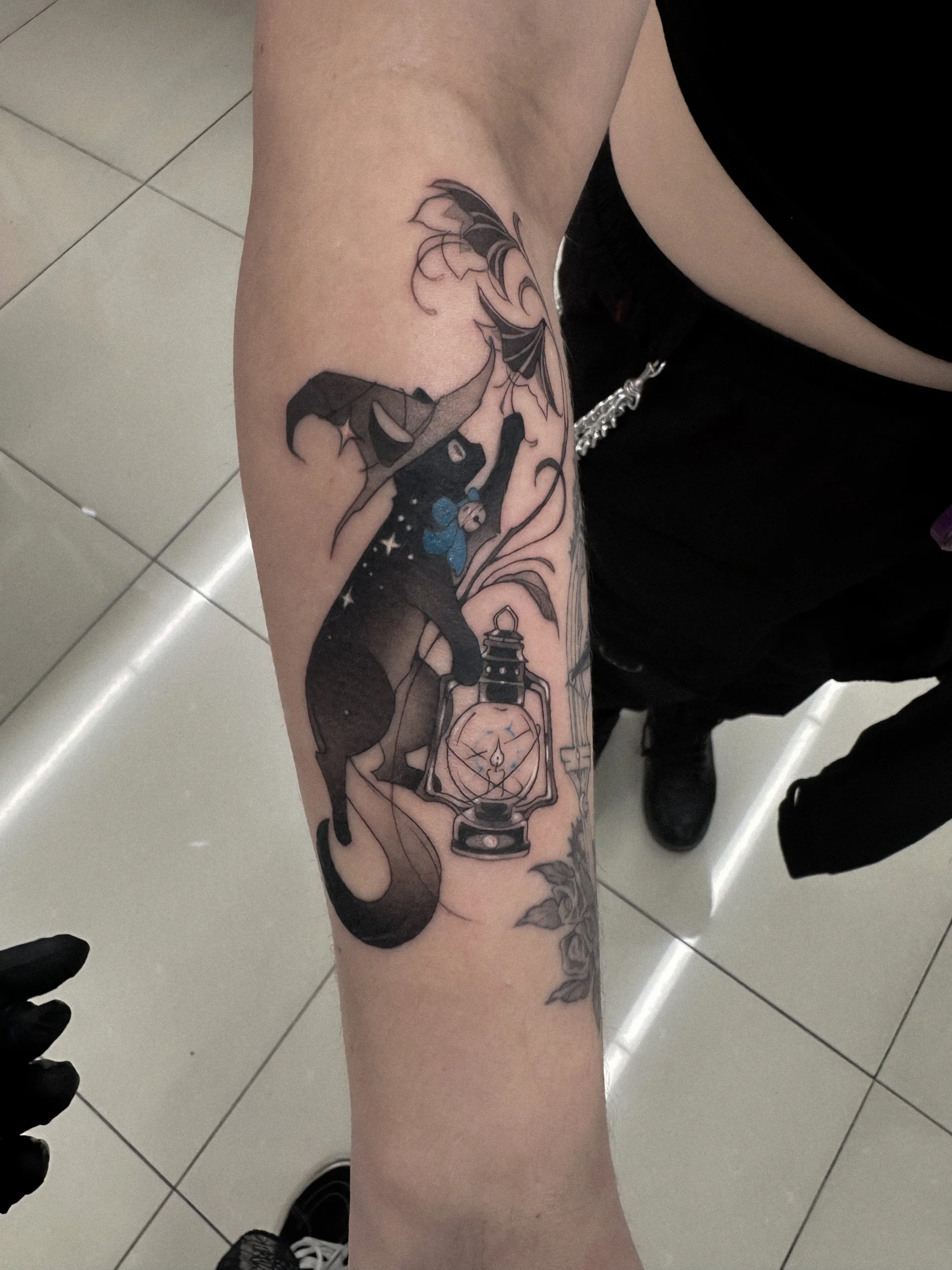 Tattoo of a butterfly, a lantern, and a clock on a person's forearm.