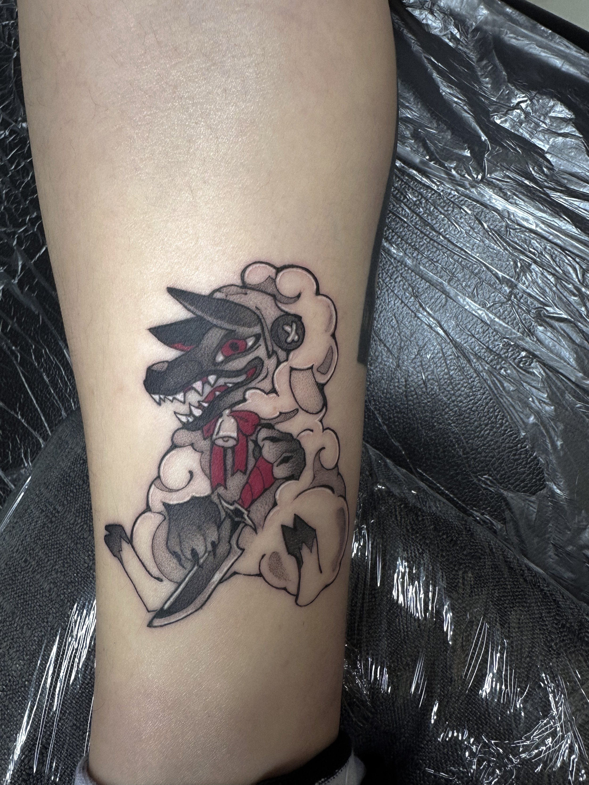 Tattoo of a fierce wolf with red eyes, sharp teeth, and a red tongue, surrounded by smoky clouds, on a person's leg.