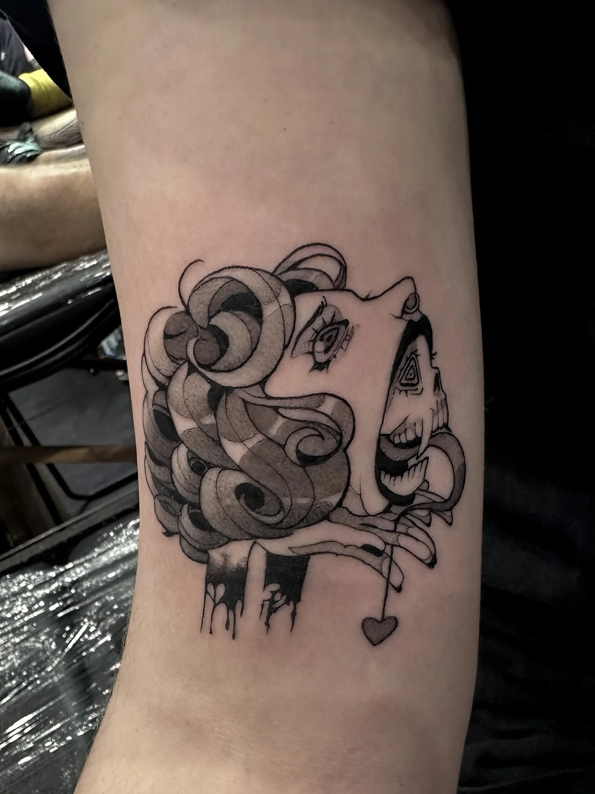Black and gray tattoo of a woman's face with flowing hair, roses, and a small heart on a person's arm.