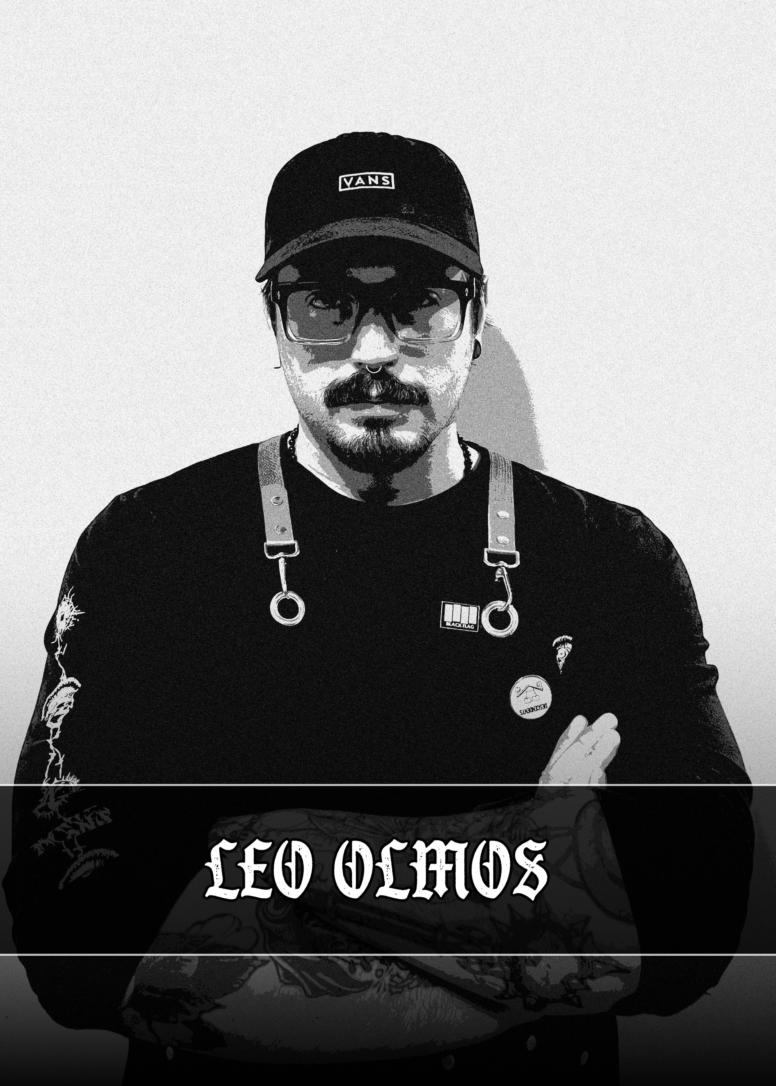 Black and white portrait of a person wearing a Vans baseball cap, glasses, and a nose ring, with tattoos on their arms, crossed arms, and a shirt with printed text.