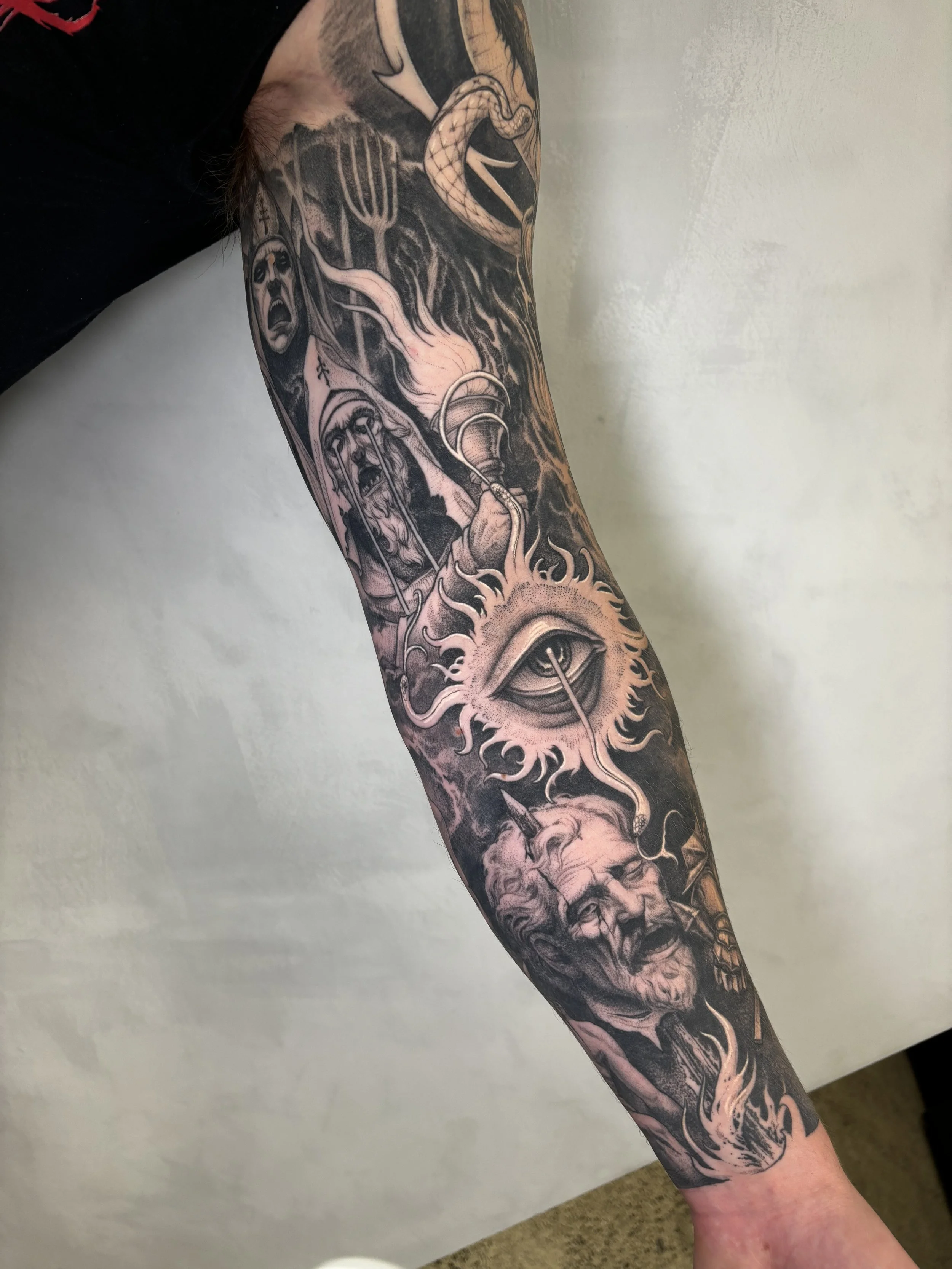 Black and gray tattoo sleeve featuring a religious figure, a large eye with rays, a screaming face, a snake, and flames.