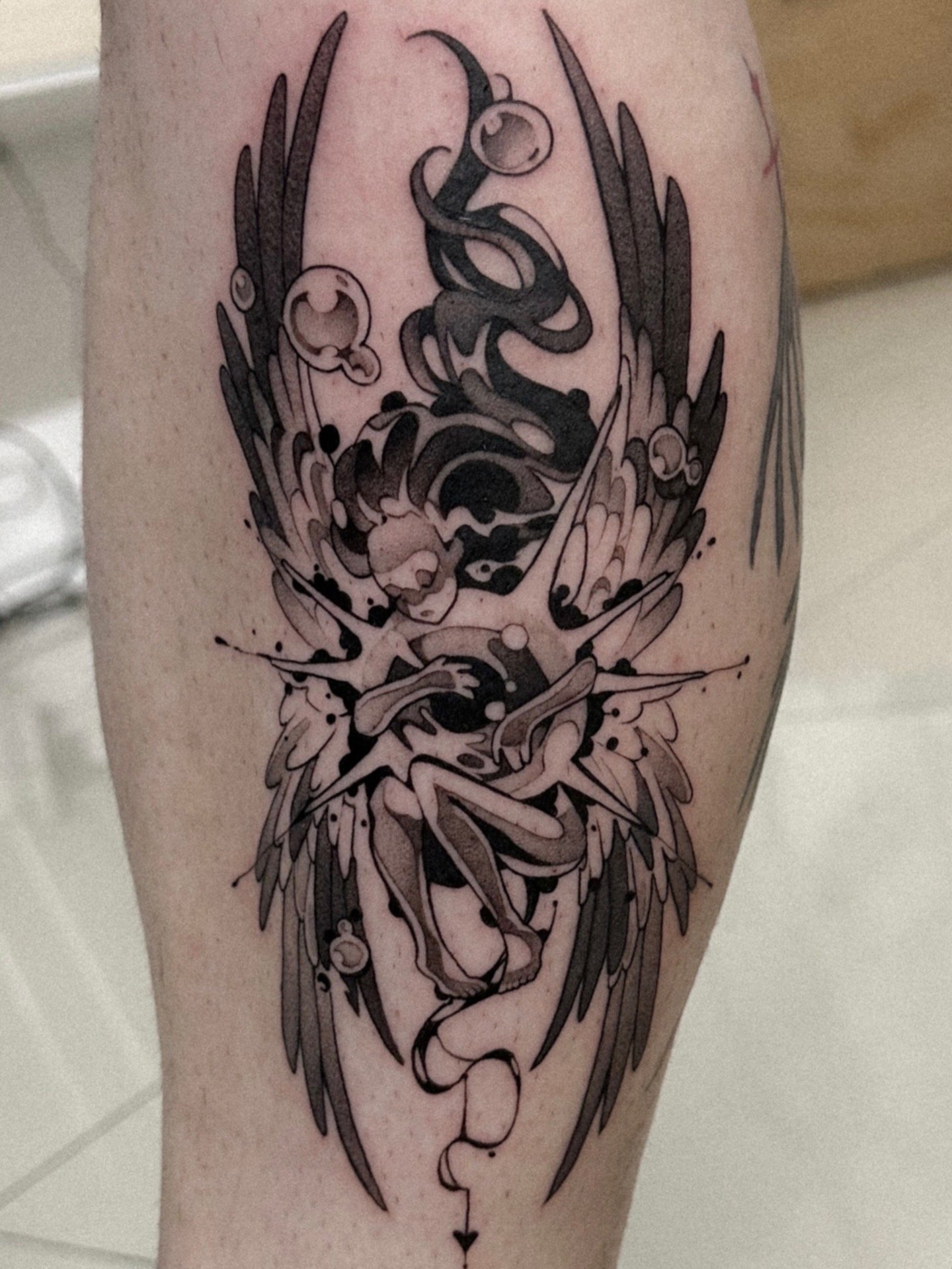 A black and gray tattoo of a fantasy creature with wings, horns, and other intricate details on a person's thigh.