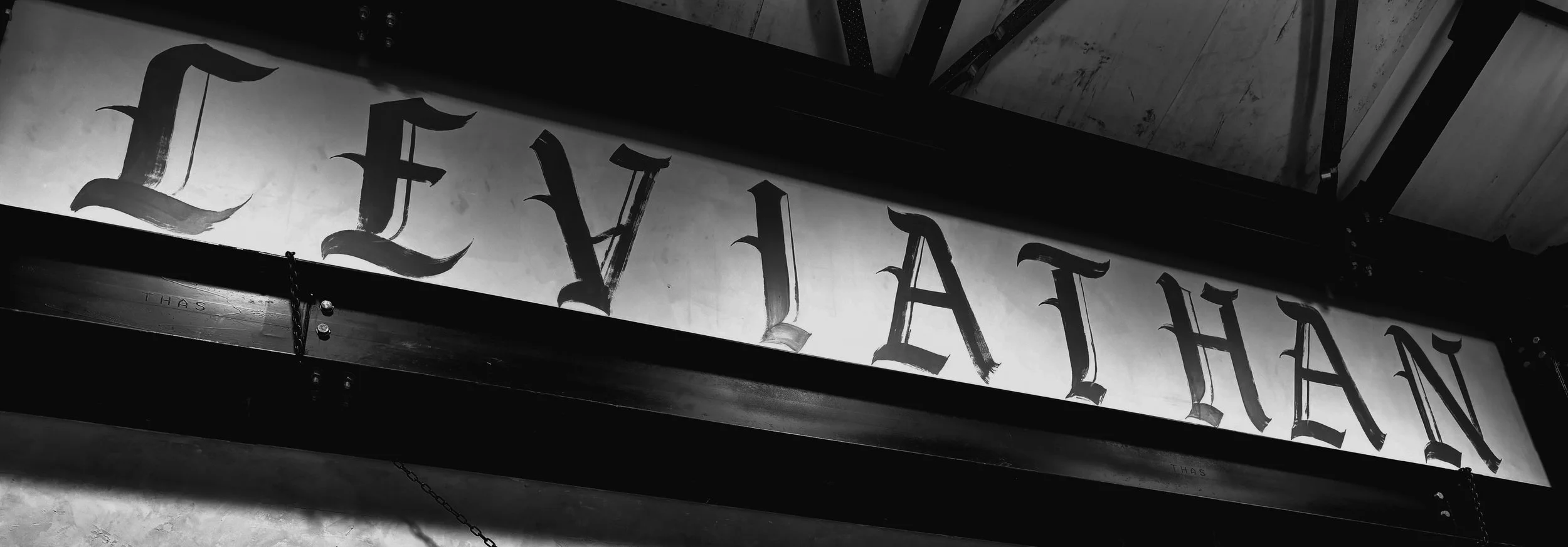 Black and white photo of a sign with large Gothic-style letters that spell 'THE LIBRARY' hanging from the ceiling.
