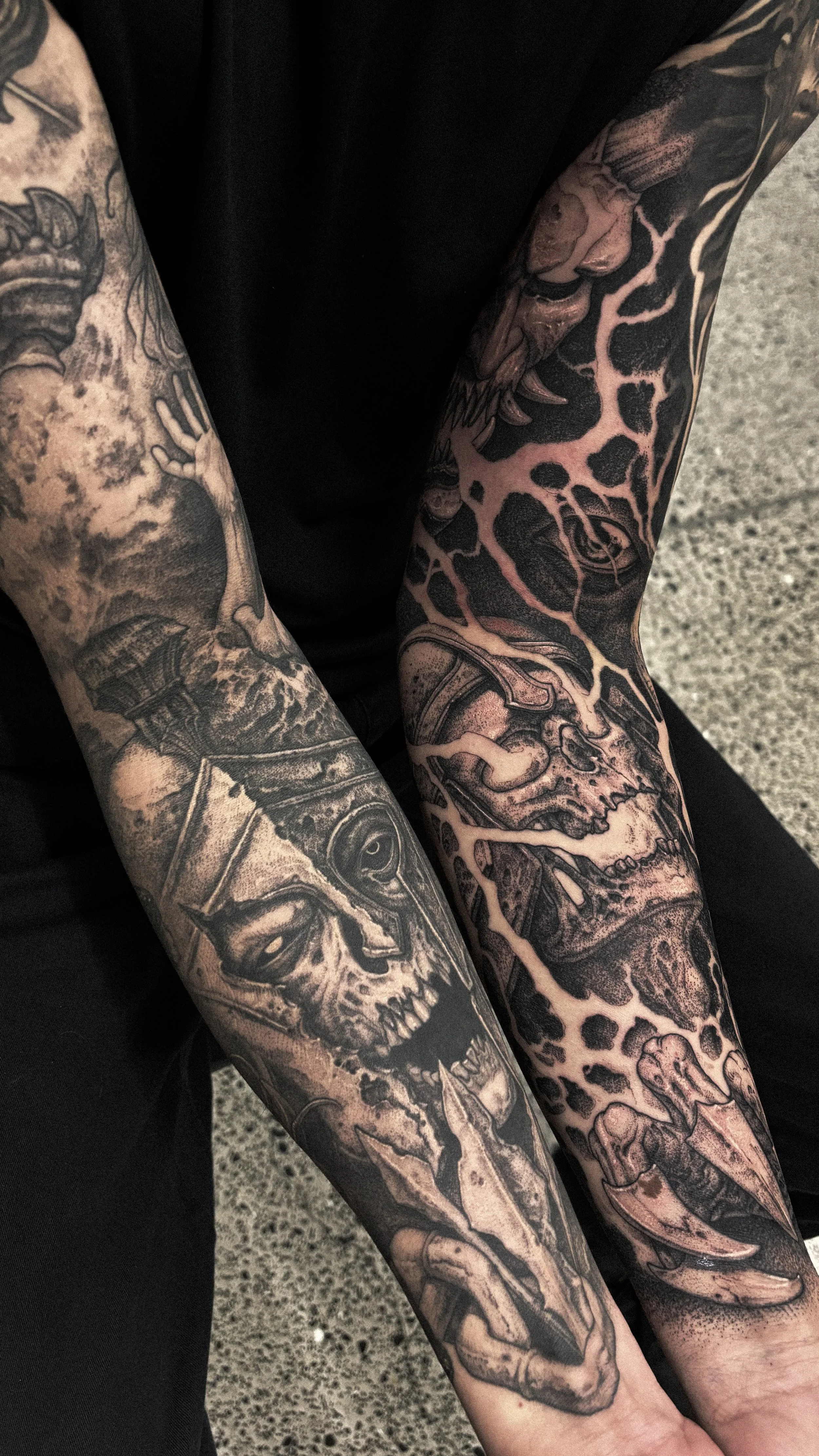 Close-up of black and gray tattoos on person's arms, featuring skulls, a tiger's face, a humanoid figure, clouds, and abstract patterns.