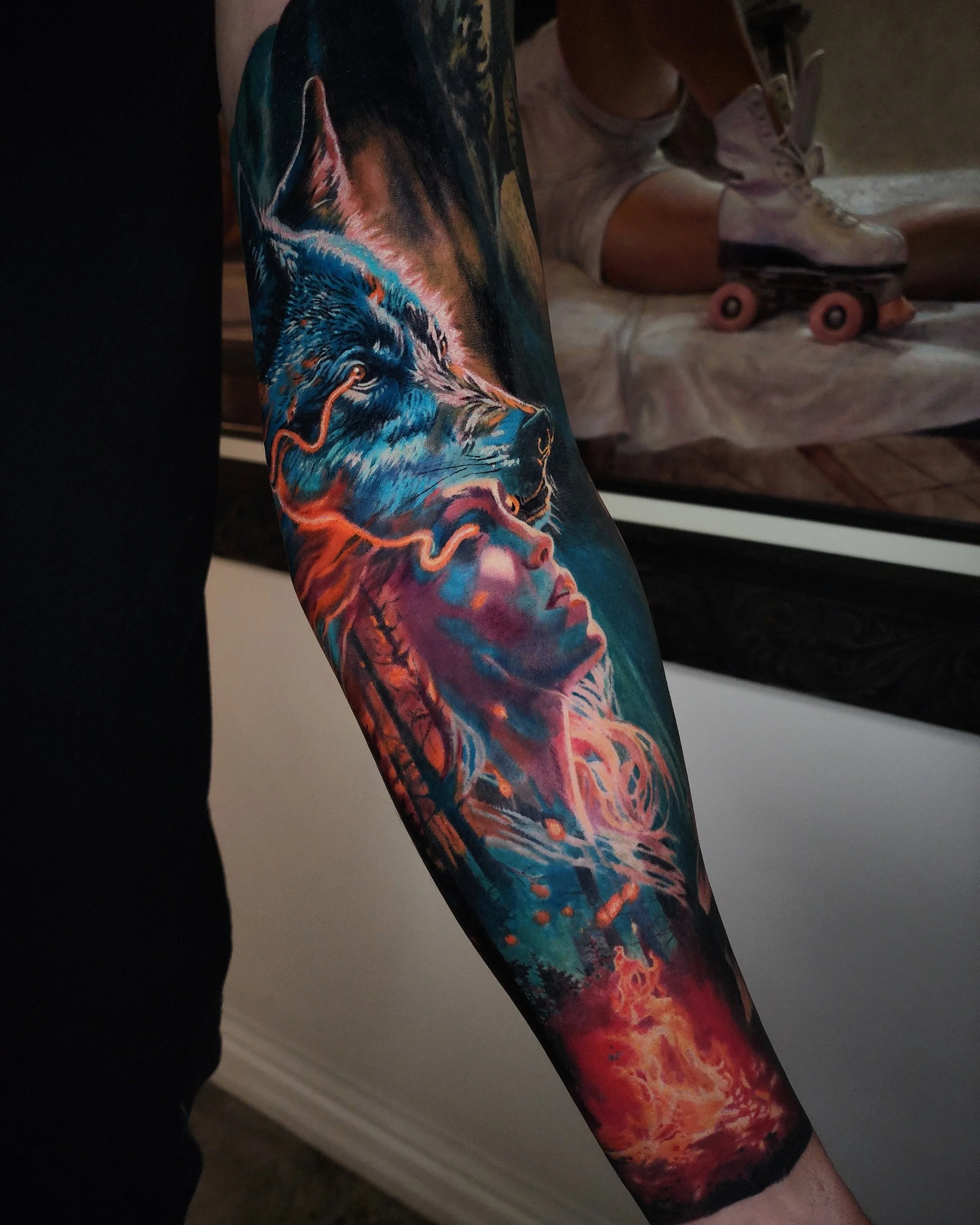 Colorful tattoo of a wolf howling and a woman's face with flowing hair on a person's arm.