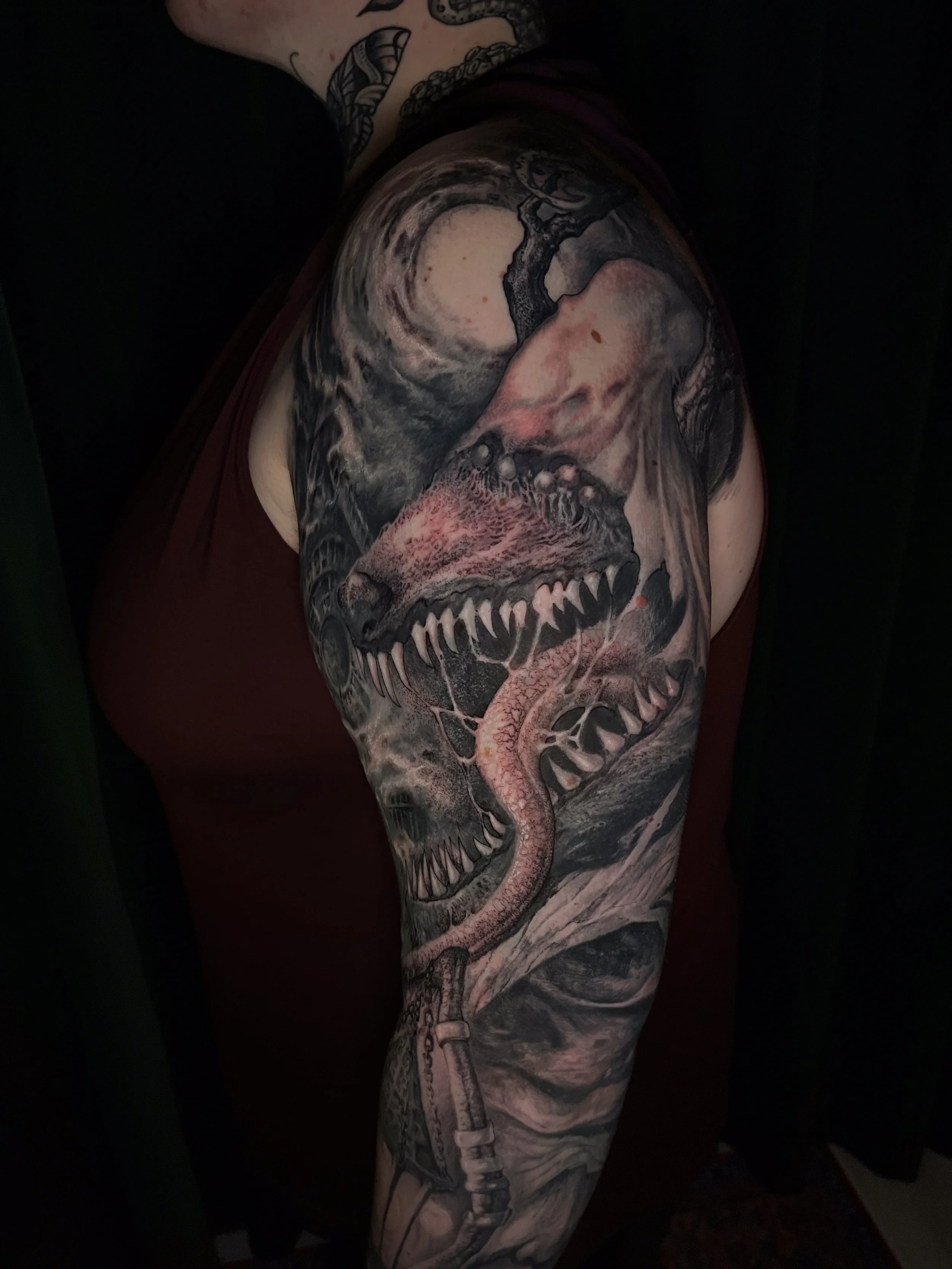 A detailed black and gray tattoo of a dinosaur skull, with sharp teeth, on a person's arm.