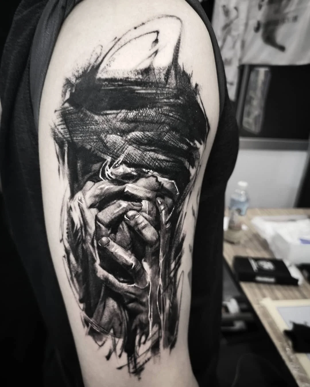 Black and gray tattoo of a person with hands covering their face, detailed with expressive brush strokes on upper arm.