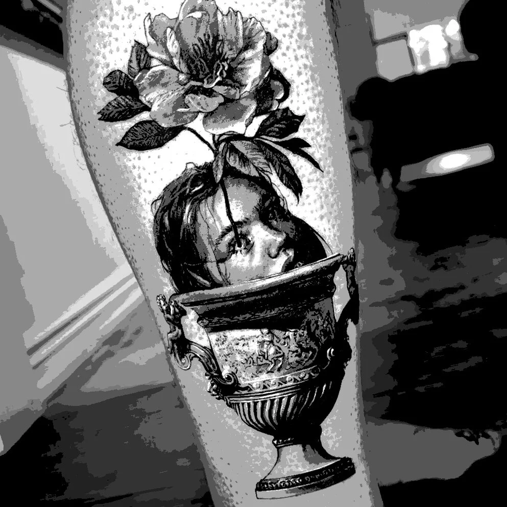 A black and white tattoo of a woman's face with glasses inside a decorative urn, topped with a large flower.