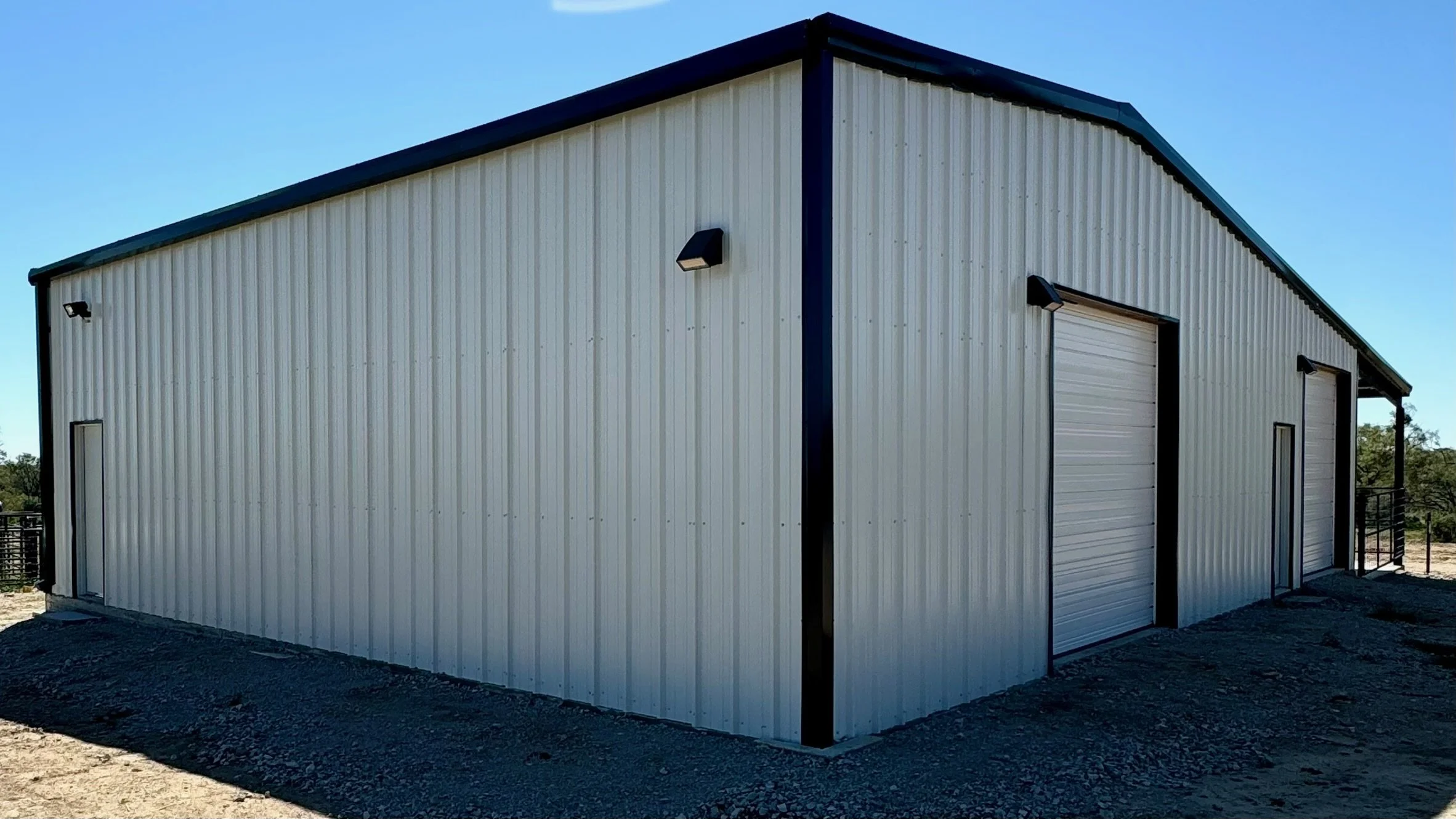 A large white metal storage building with two roll-up garage doors and small side doors, set against a clear blue sky.