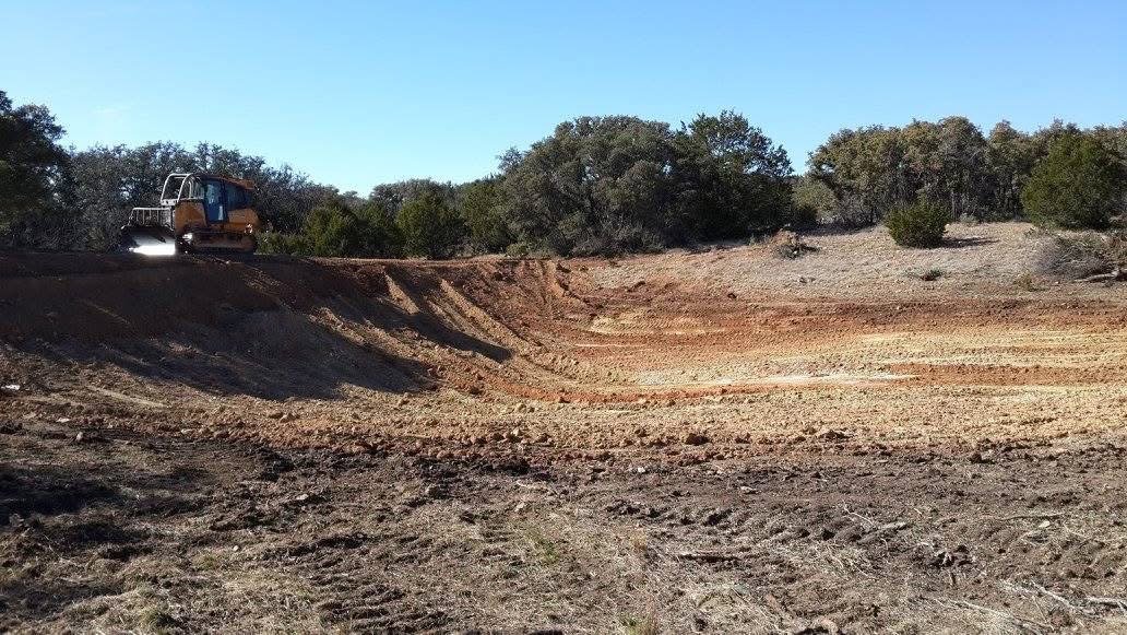 A construction vehicle, a yellow or orange bulldozer, working on a dirt road in a rural area with trees in the background.