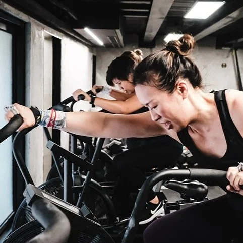 Three women exercising intensely on stationary bikes in a gym with a modern industrial design.