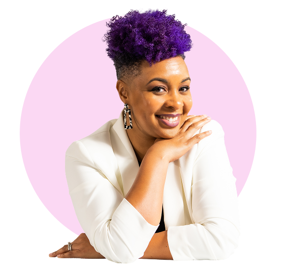 Smiling woman with purple curly hair, wearing a white blazer and earrings, resting her chin on her hand in front of a pink circular background.
