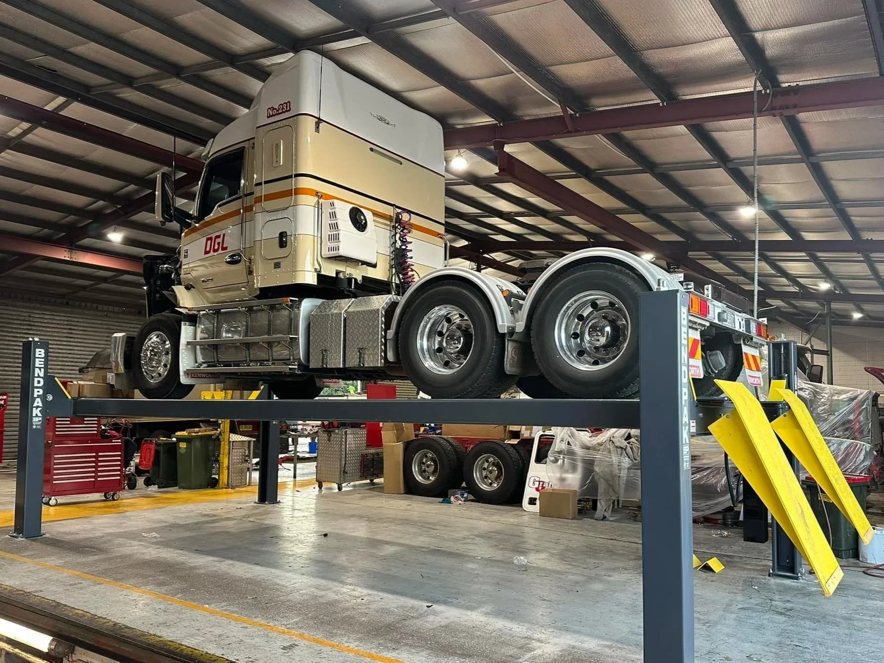 A semi-truck cab mounted on a vehicle maintenance lift inside a garage or workshop.