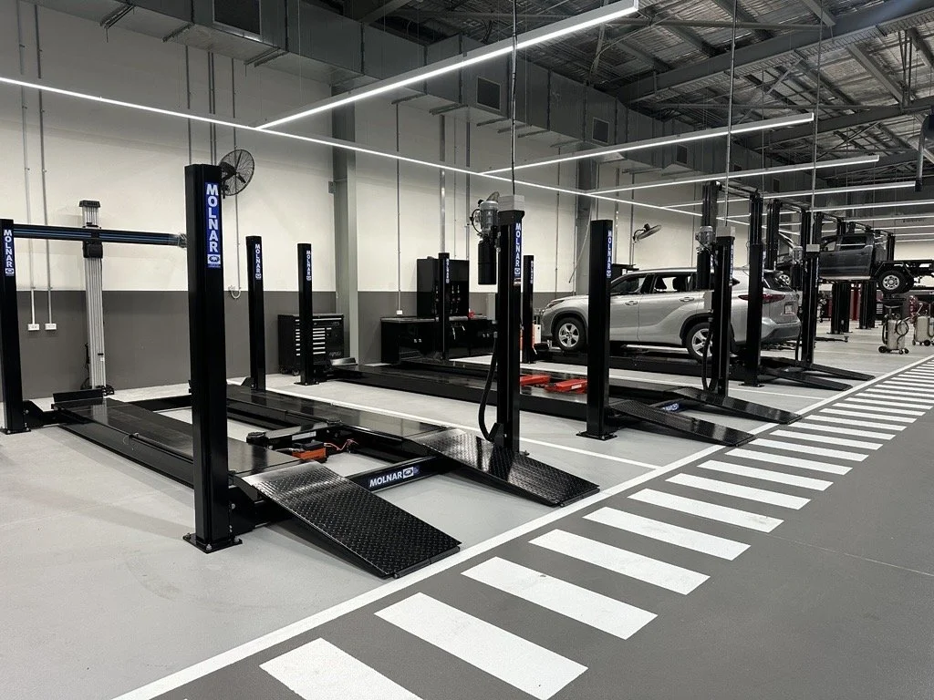 An automotive workshop with multiple vehicle lifts, some with cars, and a striped pedestrian crossing in the foreground.