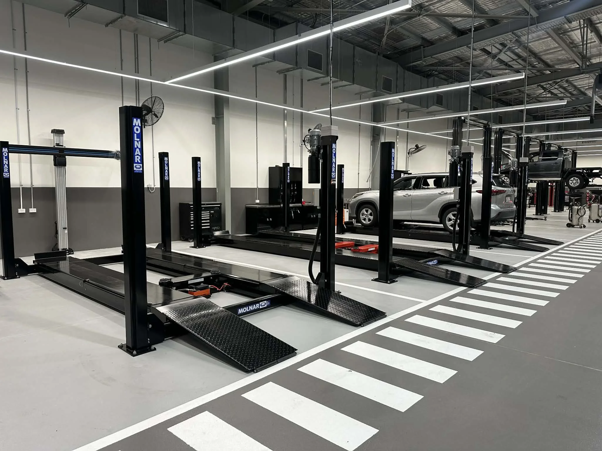 Empty automotive workshop with vehicle lifts, a silver SUV on one lift, tools, and equipment.
