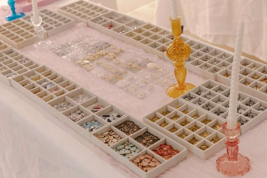 Jewelry display with organized trays of rings, earrings, and small accessories, decorated with two pink and yellow candle holders.