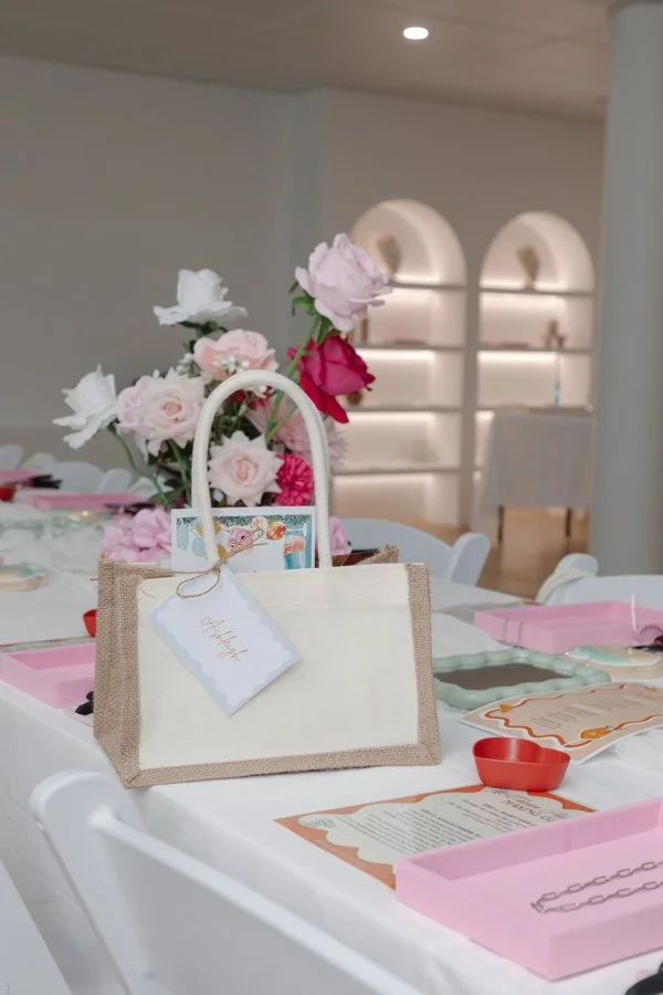 Table decorated with pink and white flowers, gift bags, and pink boxes in a pastel-themed setting.
