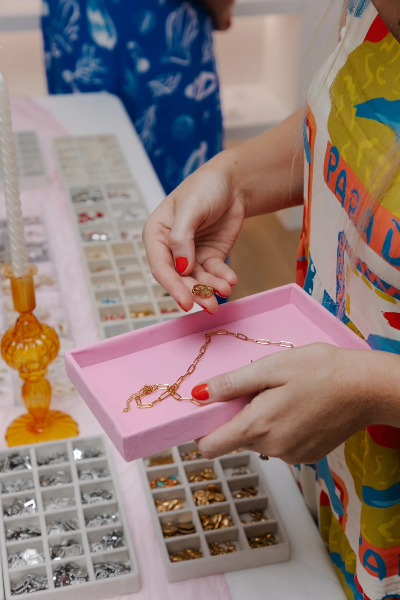 Person holding a gold necklace with a pink jewelry tray in a jewelry store, with various rings and jewelry displayed on the table.