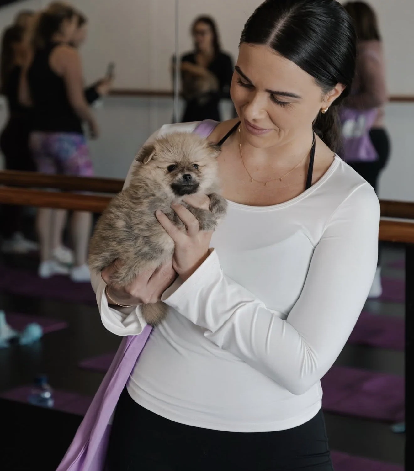 A woman holding a small fluffy puppy in a yoga or fitness studio.