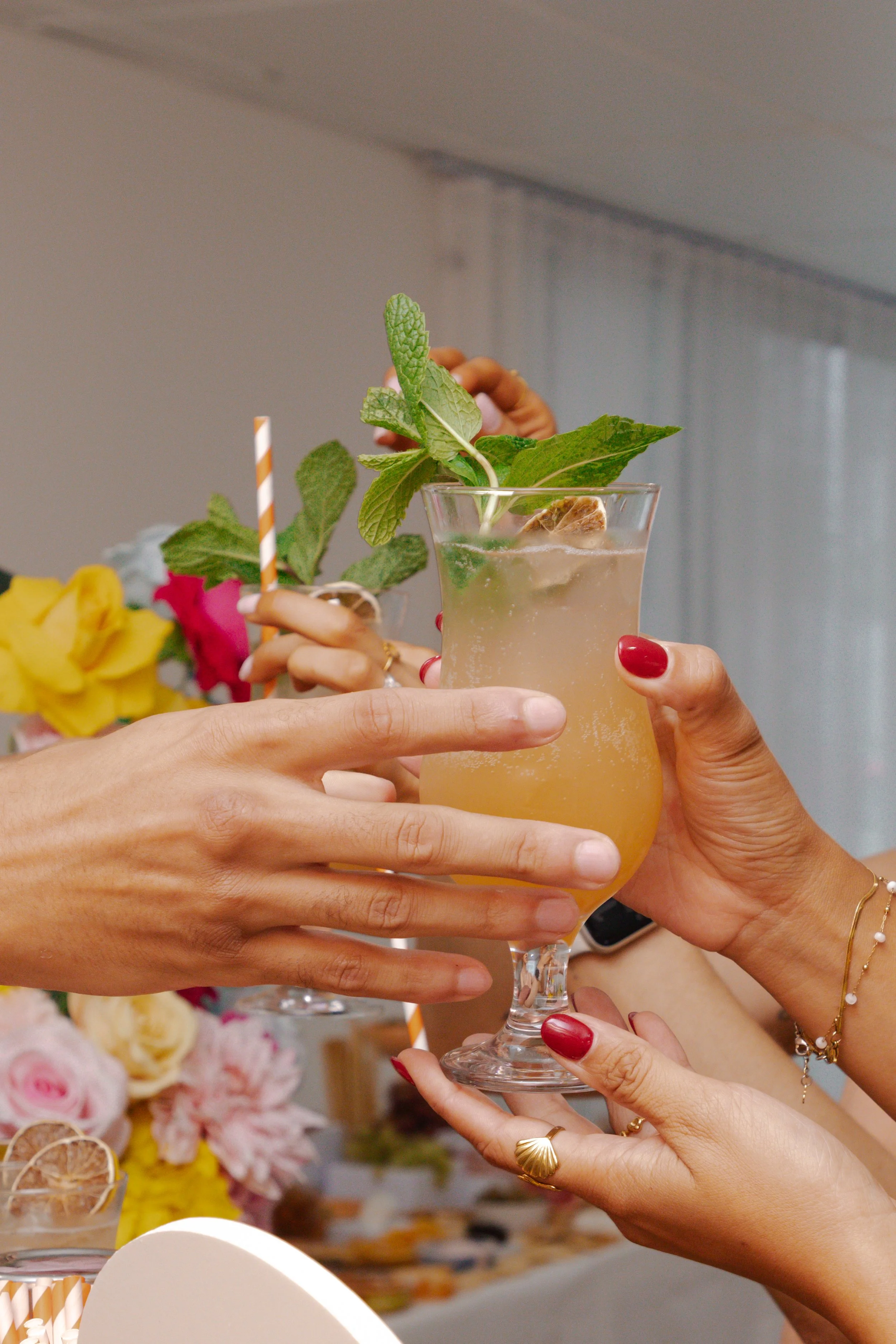 People clinking glasses with a tropical cocktail garnished with mint and a straw, celebrating at a party or gathering.