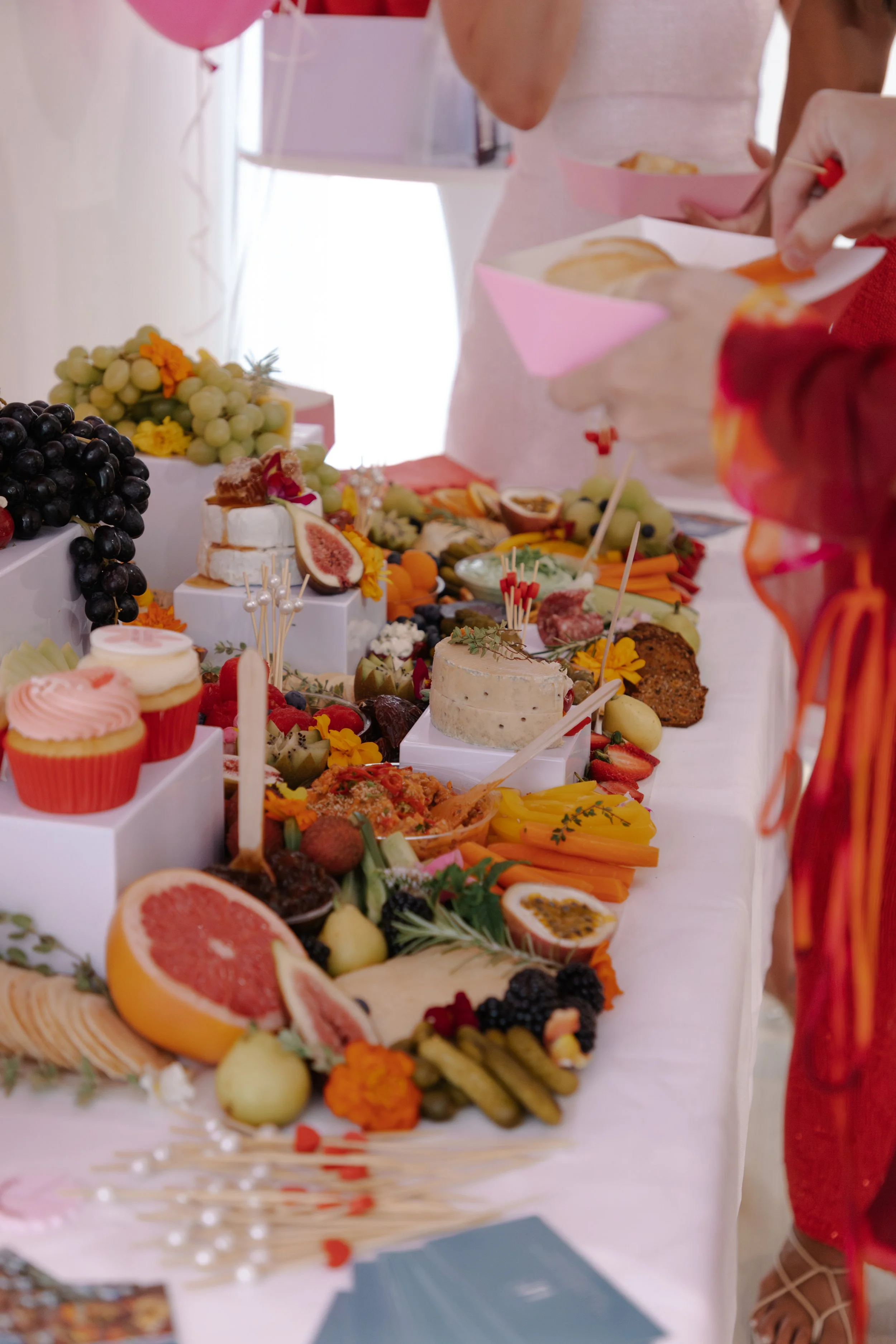 A variety of desserts, fruits, and appetizers on a long white table at a celebratory event, with people serving themselves.