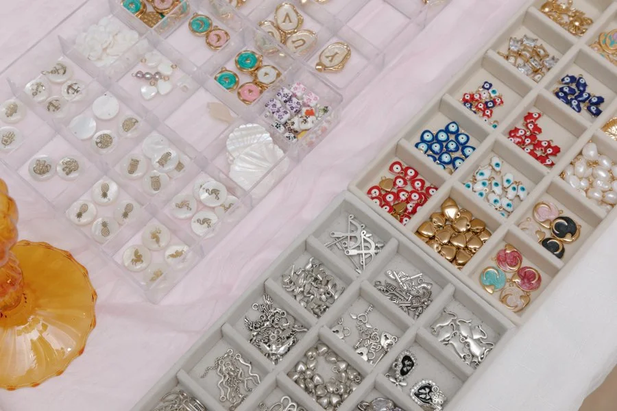 Organized jewelry charms and decorative pins in small compartments, featuring various designs and colors.
