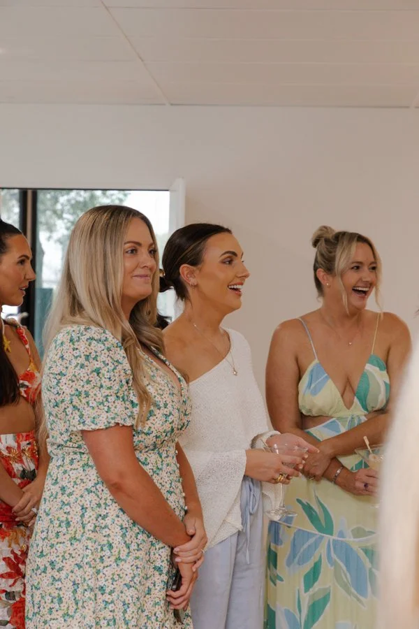 Four women standing indoors, smiling, and engaged in conversation at a social event or gathering.