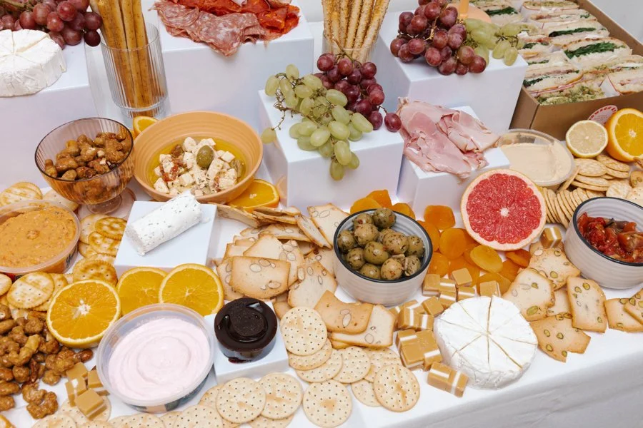 A variety of cheeses, crackers, grapes, citrus fruits, nuts, and spreads displayed on a table for a charcuterie board.