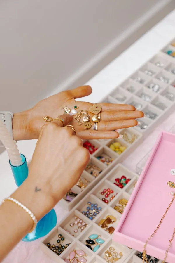 Person organizing gold, silver, and colorful jewelry and rings in a jewelry box container on a table.