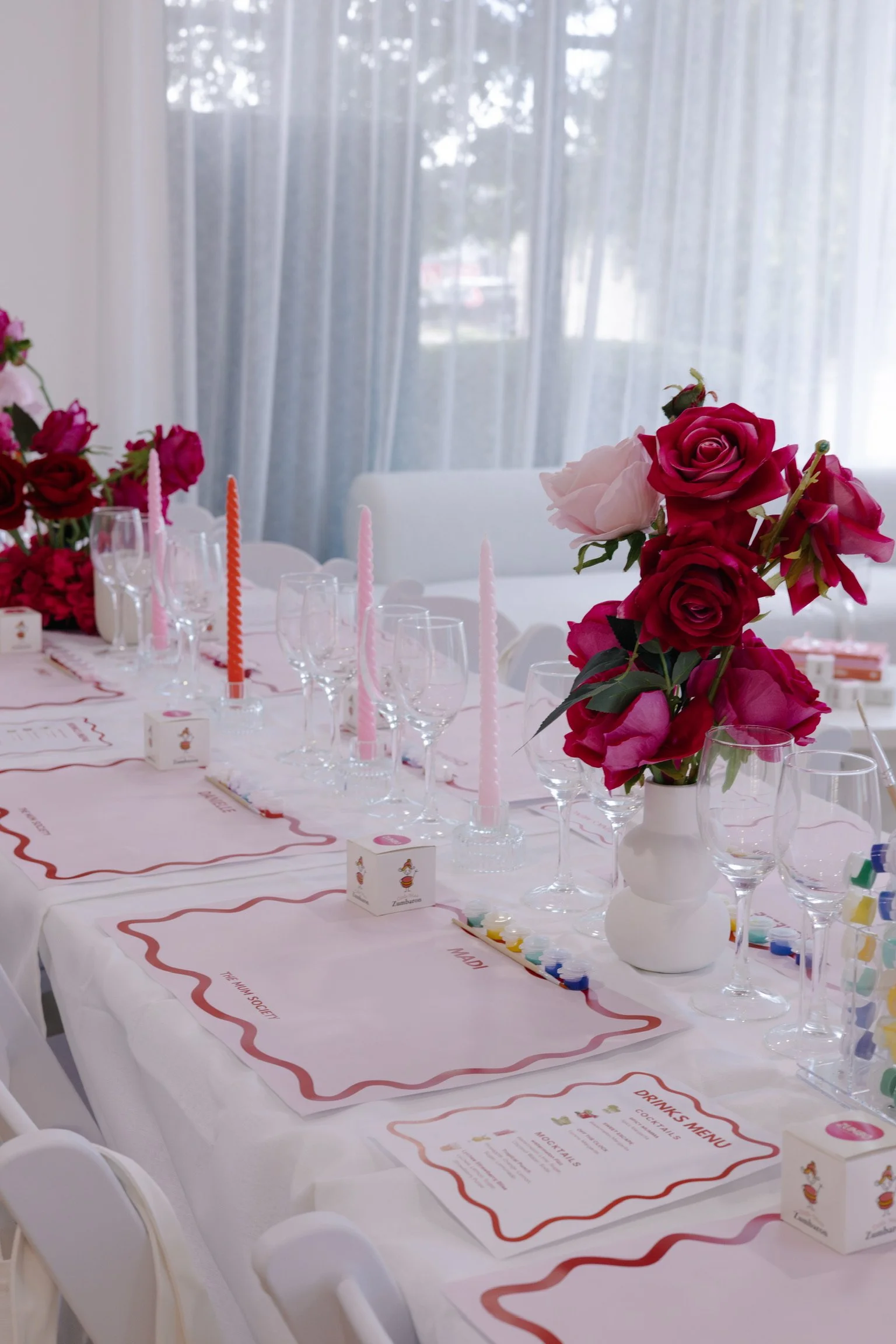 Decorated table with pink and red roses, pink candles, wine glasses, and party favors for a celebration or party.