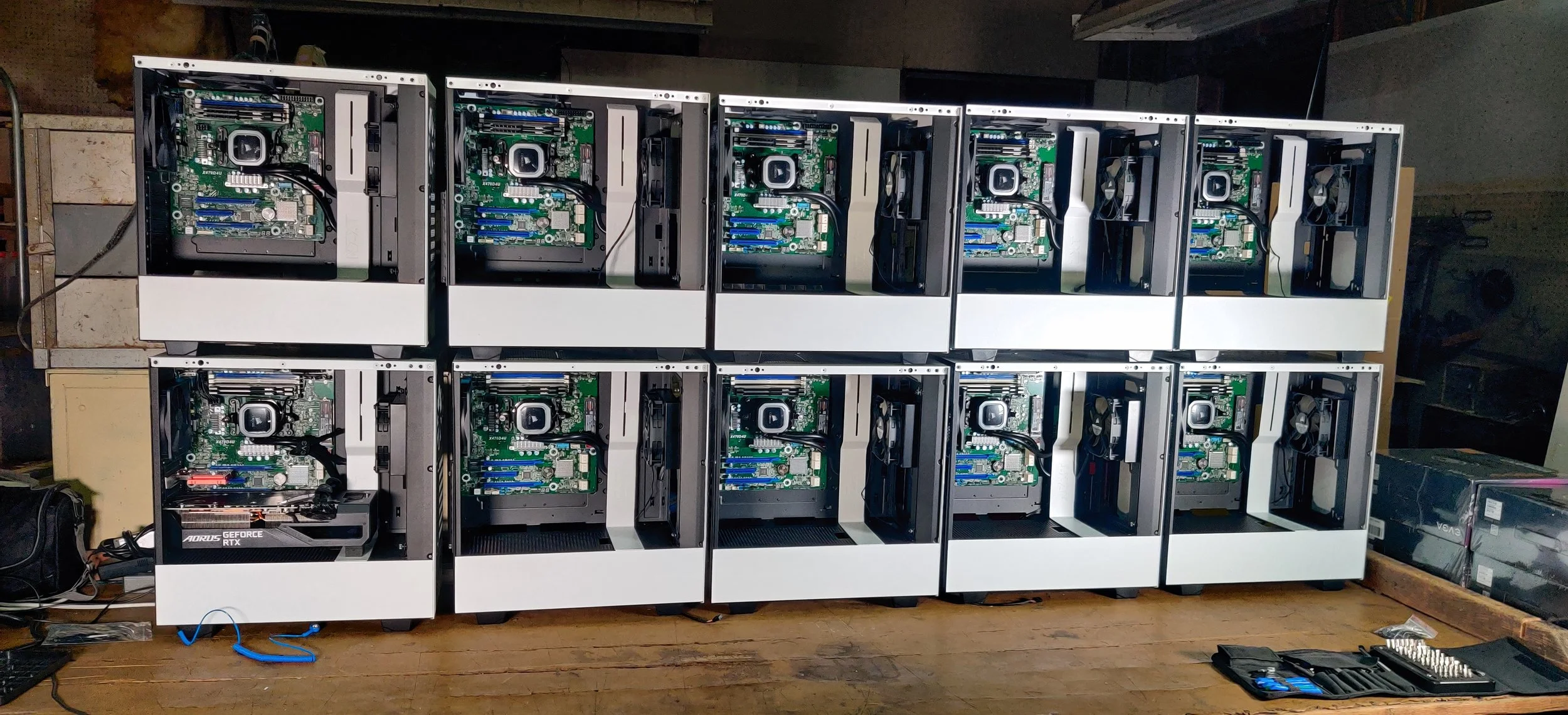 Multiple open computer cases showing motherboards, cooling fans, and graphics cards, arranged on a wooden workbench in a workshop.